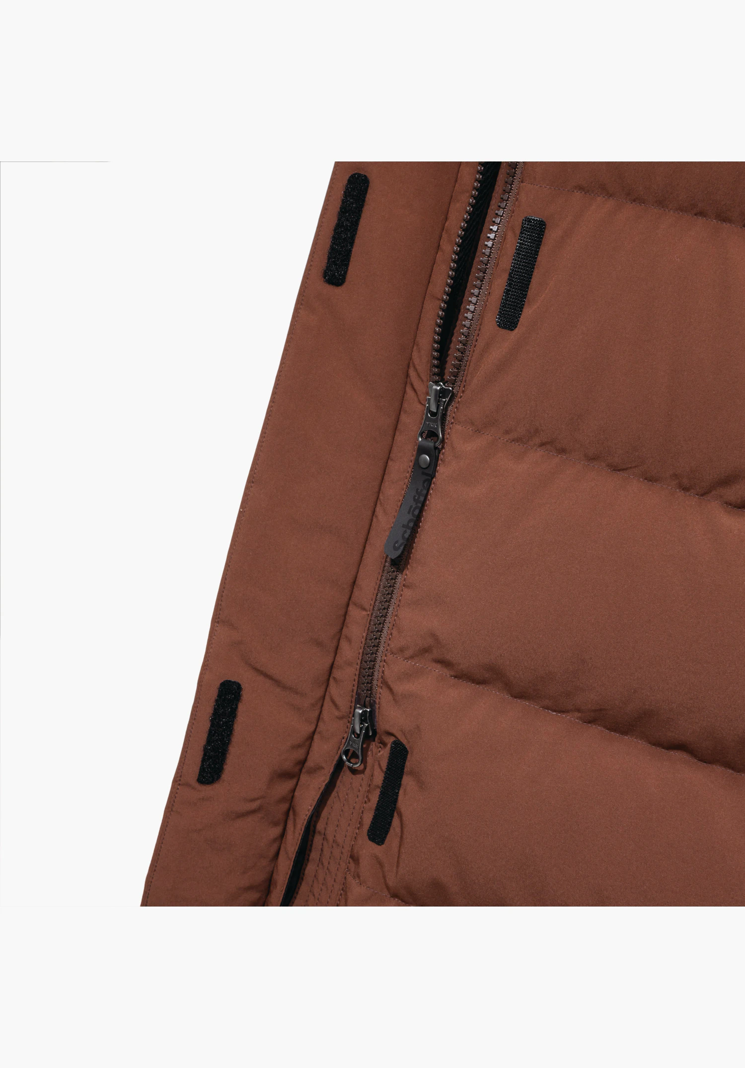 Down Coat Style Vindave WMS. Gedetailleerd aanzicht van de bruine 2-wegrits met Schöffel-opschrift op de trekker en klittenbandsluitingen op de overslag. Close-up voor een witte/neutrale achtergrond.