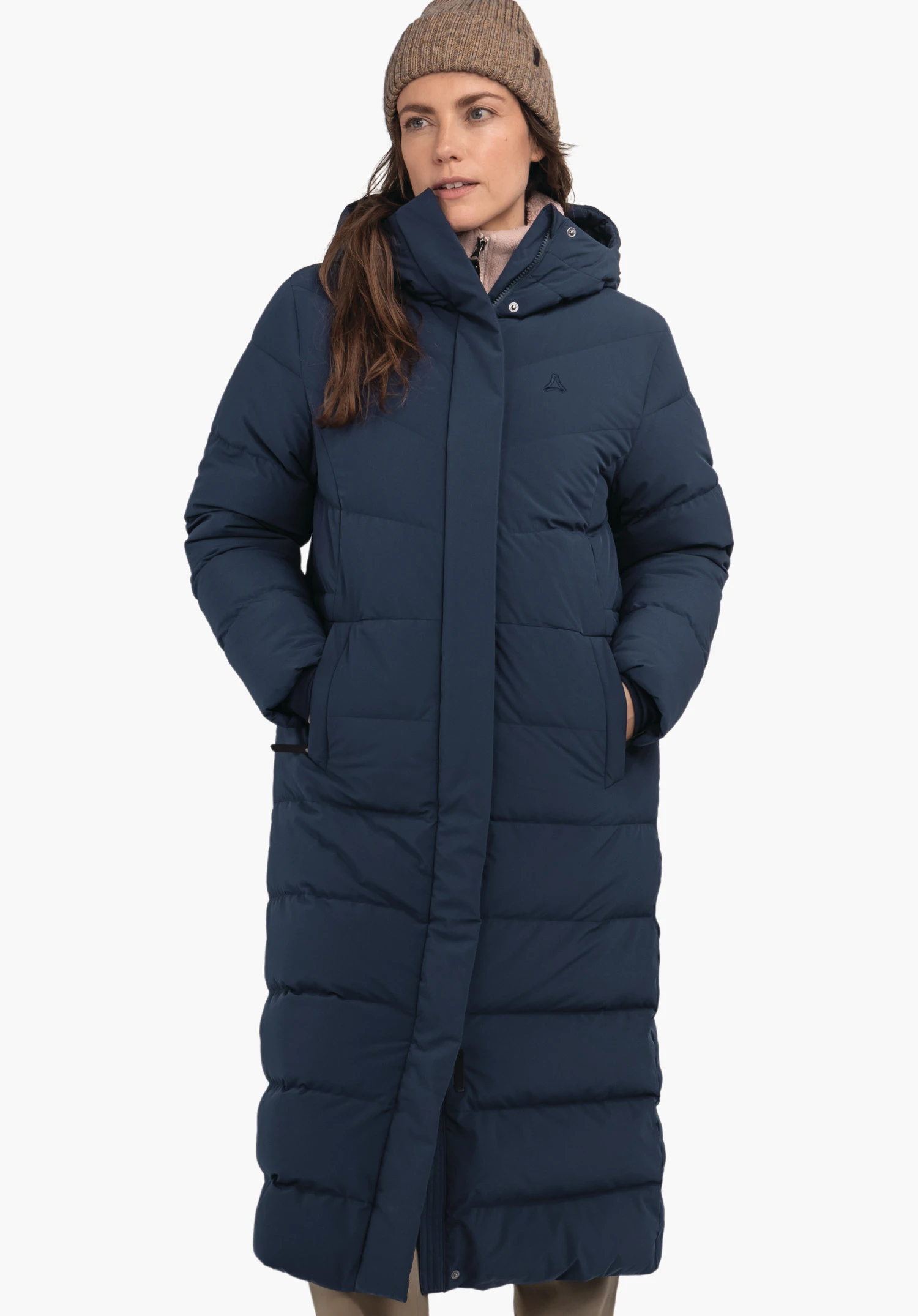 Down Coat Style Vindave WMS dark blue quilted coat worn by a woman; high-closing collar and hood, hands in pockets; visible Schöffel logo on the chest; white background.
