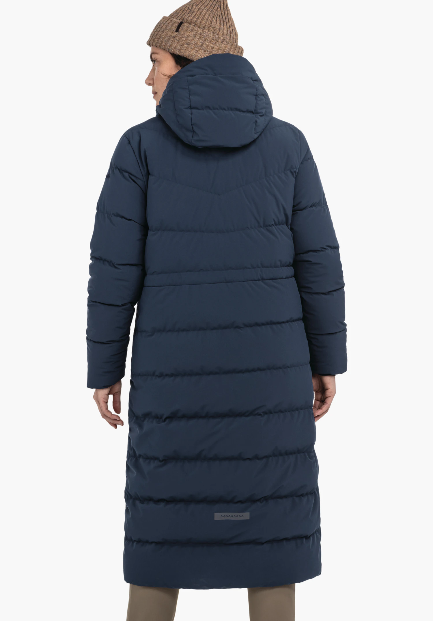 Down Coat Style Vindave WMS lange donkerblauwe gewatteerde mantel, gedragen door een persoon met de rug naar de camera; capuchon opgezet, muts zichtbaar, neutrale lichte achtergrond.