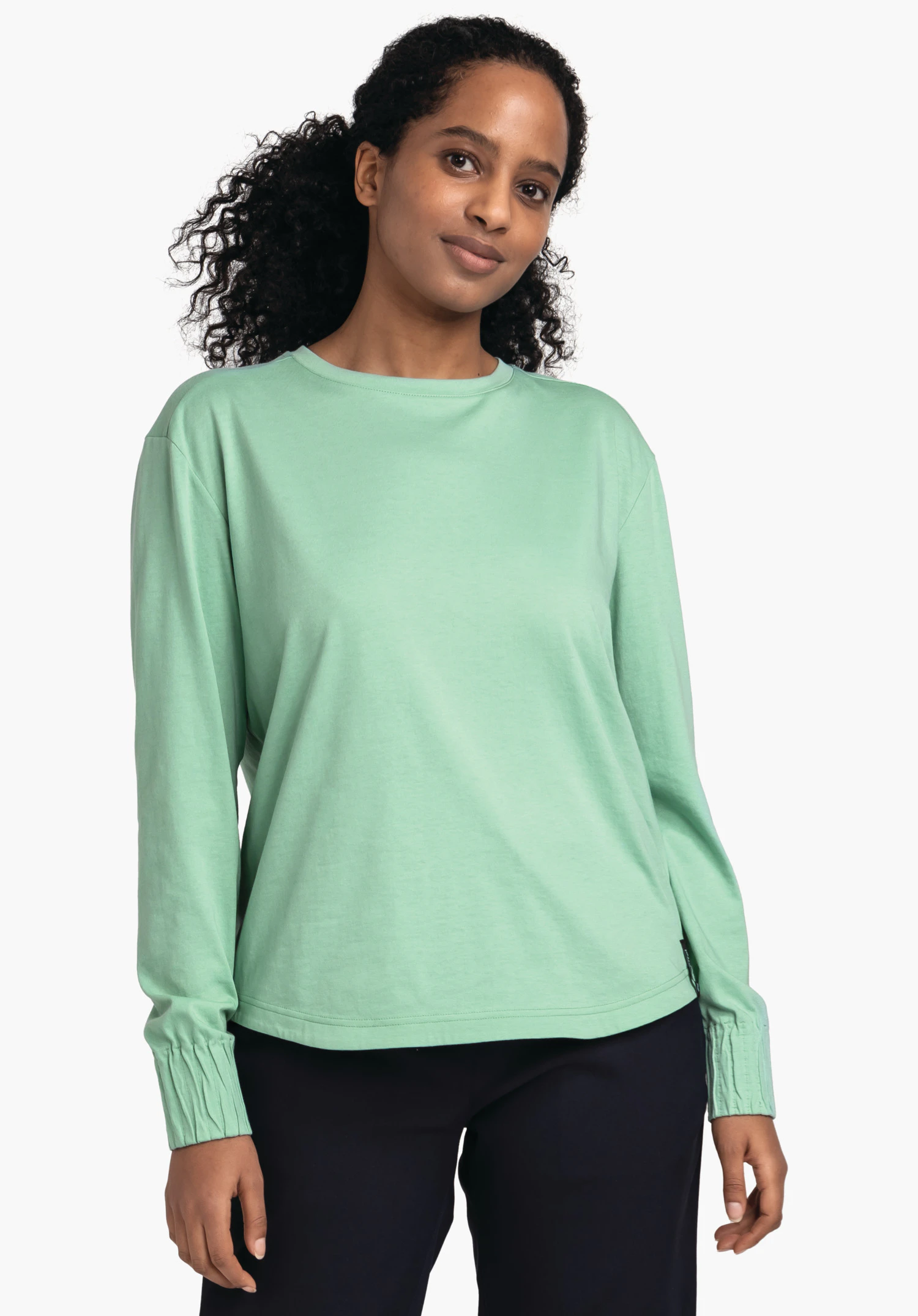 Longsleeve Style Collada WMS haut manches longues vert clair porté ample par une personne debout; regard légèrement de côté, pantalon bleu foncé; fond studio blanc.