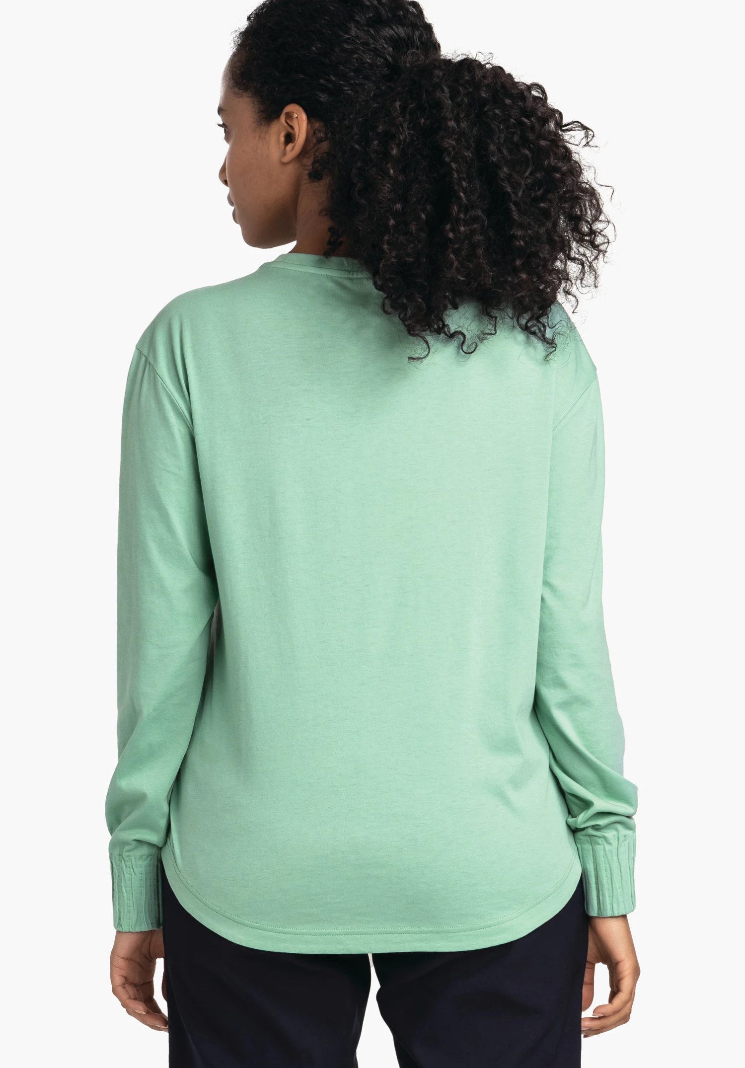 Longsleeve Style Collada WMS t-shirt manches longues vert clair porté de dos; bras détendus, tête tournée sur le côté; fond blanc, pantalon bleu foncé, cheveux noirs bouclés.