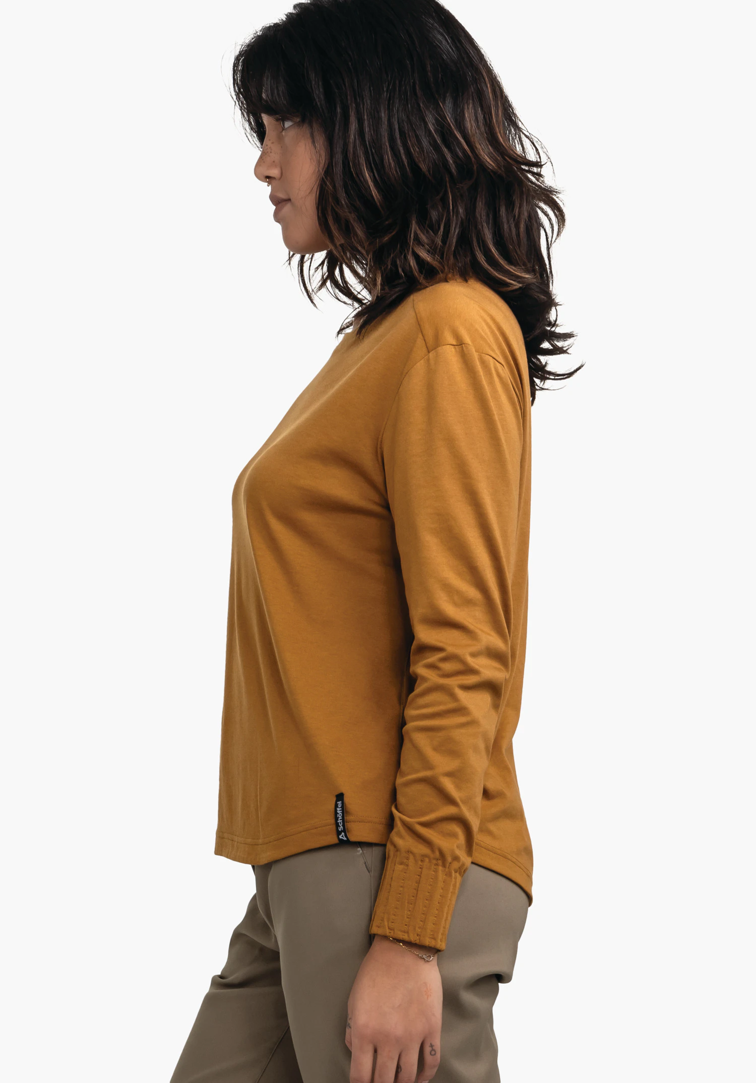 Longsleeve Style Collada WMS t-shirt manches longues jaune foncé porté par une femme en profil; elle reste immobile, porte un pantalon marron clair, cheveux brun foncé ondulés, fond blanc neutre.