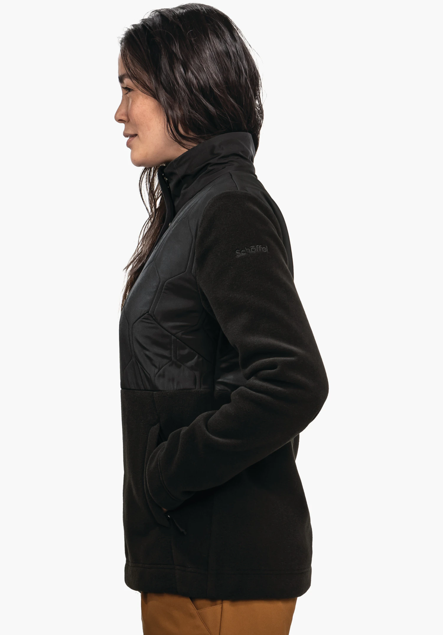 Fleece Jk Style Gregale WMS vrouw draagt een zwarte jas met opstaande kraag, staat in profiel met handen in de zakken; neutrale achtergrond. Tekst op de mouw: "schöffel".