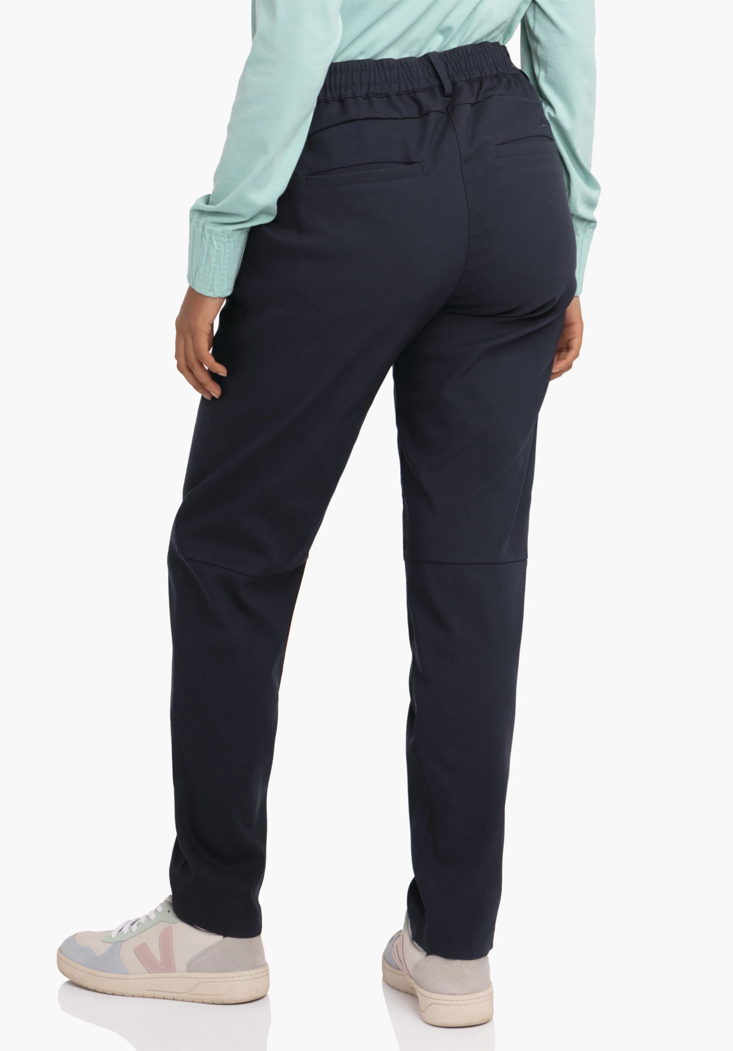 Pants Style Oaktree WMS dark blue trousers worn from the back; person stands with legs slightly apart, hands relaxed at the sides; light green top, light grey trainers; white studio background.