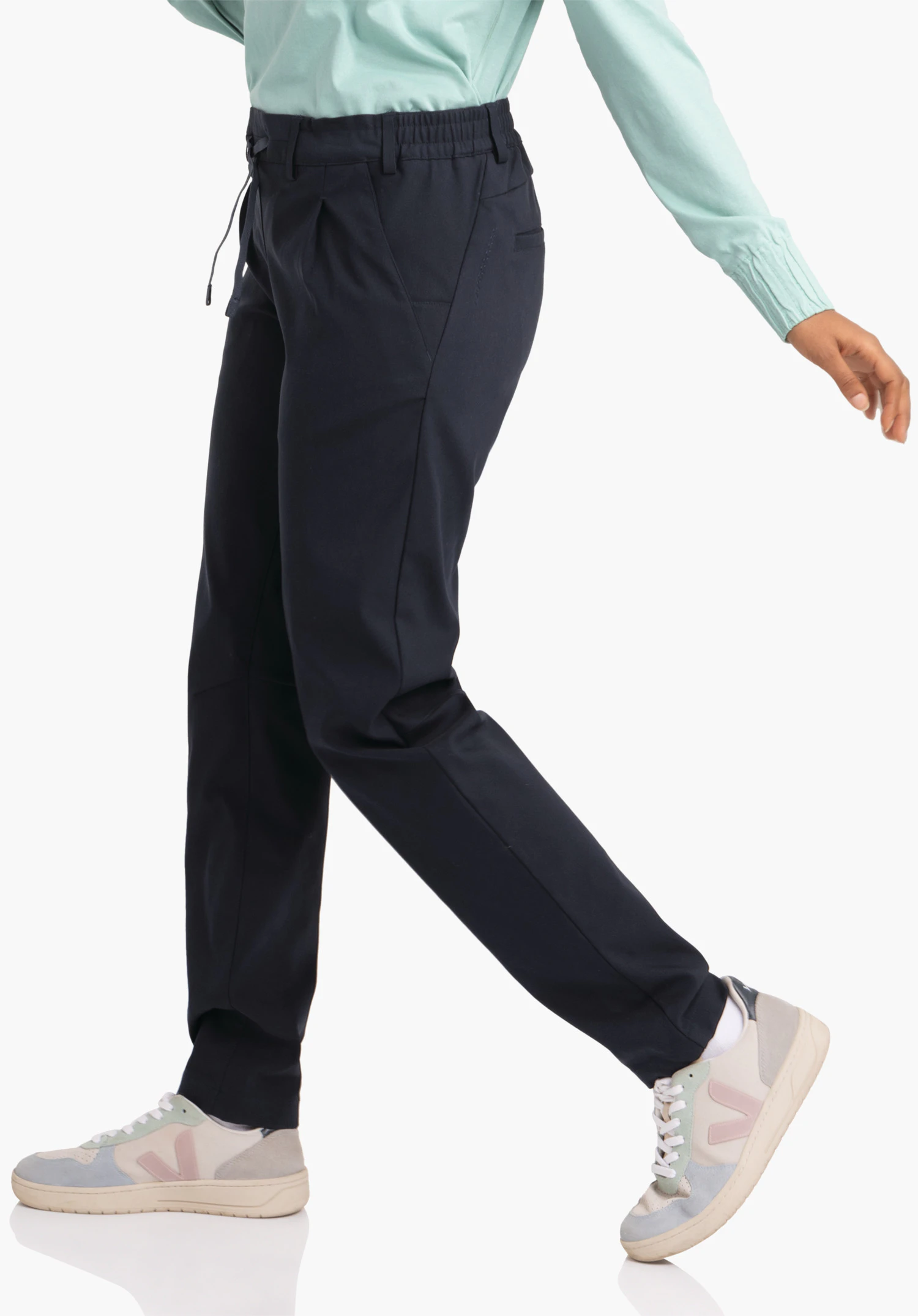 Pants Style Oaktree WMS dark blue trousers; person walks in front of a white background, wearing a light green top and light grey trainers with pink details.