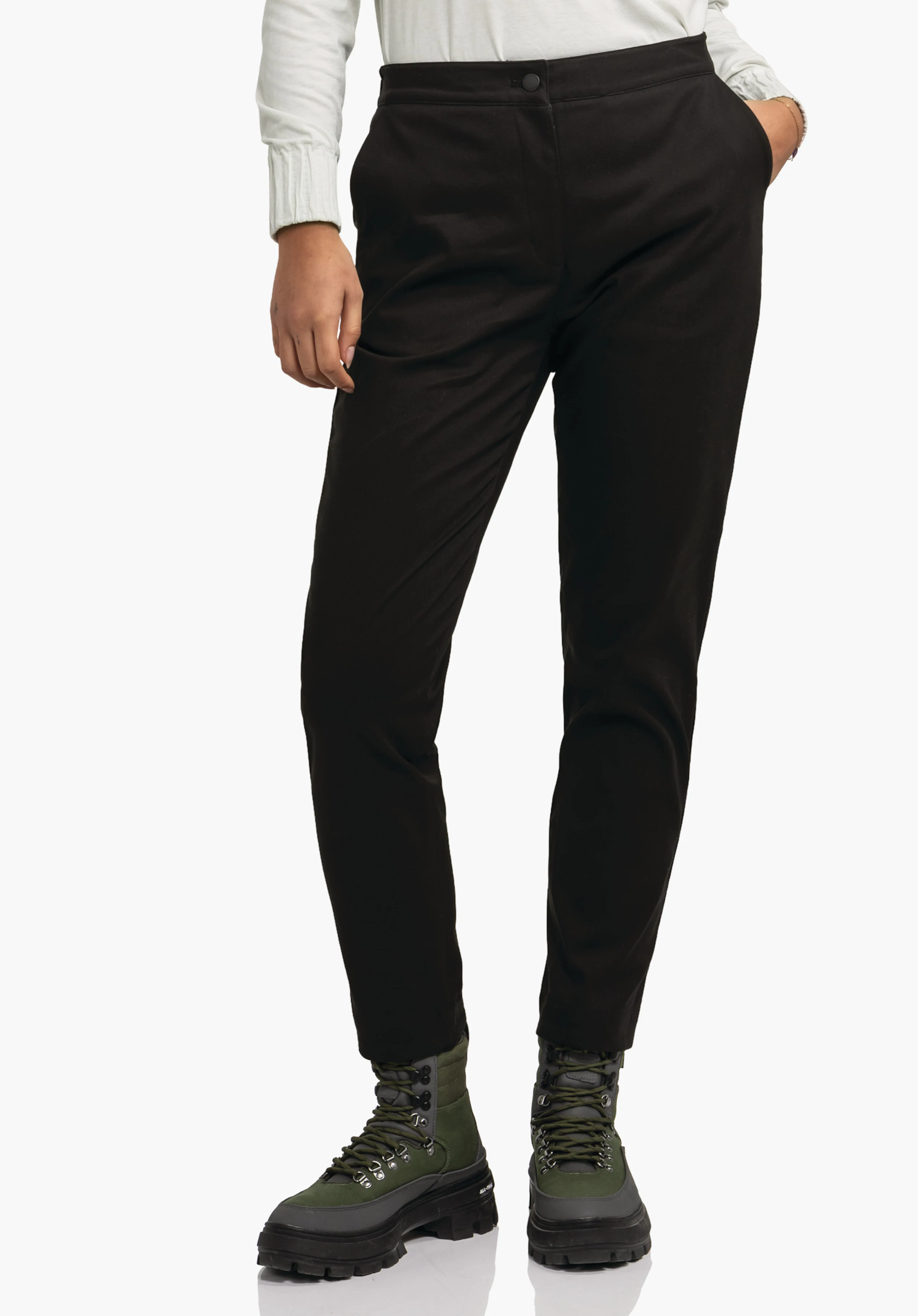 Pants Style Zourga WMS Schwarze Hose, tailliert, steht gerade; Person hat eine Hand in der Hosentasche; heller Hintergrund; dunkelgrüne Bergstiefel mit schwarzen Sohlen sichtbar.
