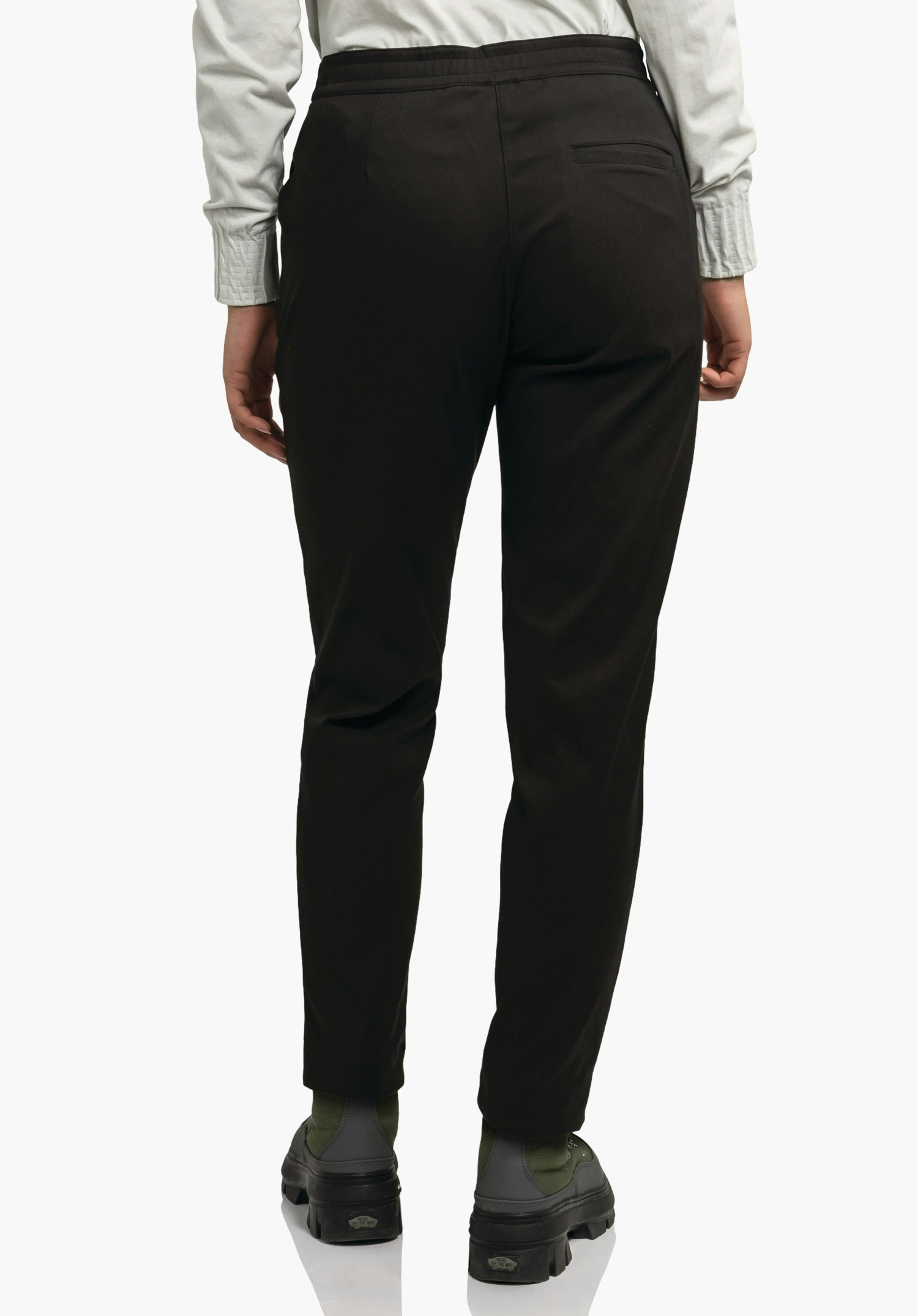 Pants Style Zourga WMS pantalon noir, porté de dos; personne debout devant un fond clair, haut blanc clair et chaussures noir-vert.