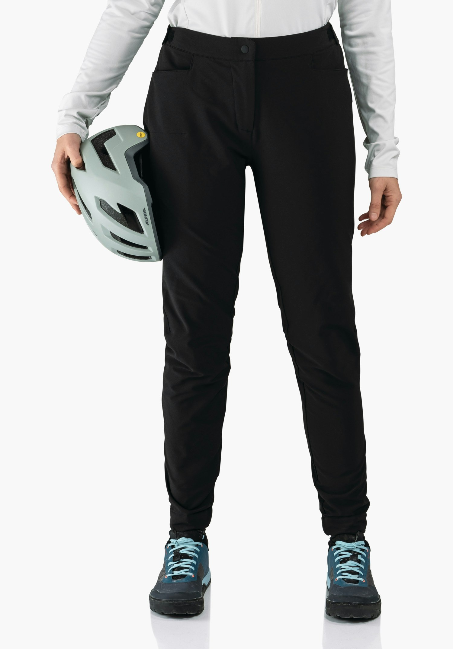 Pants Style Kubena WMS black trousers; person holds a light grey bicycle helmet with ALPINA lettering, wearing a white long-sleeve top and dark blue shoes; light plain background.
