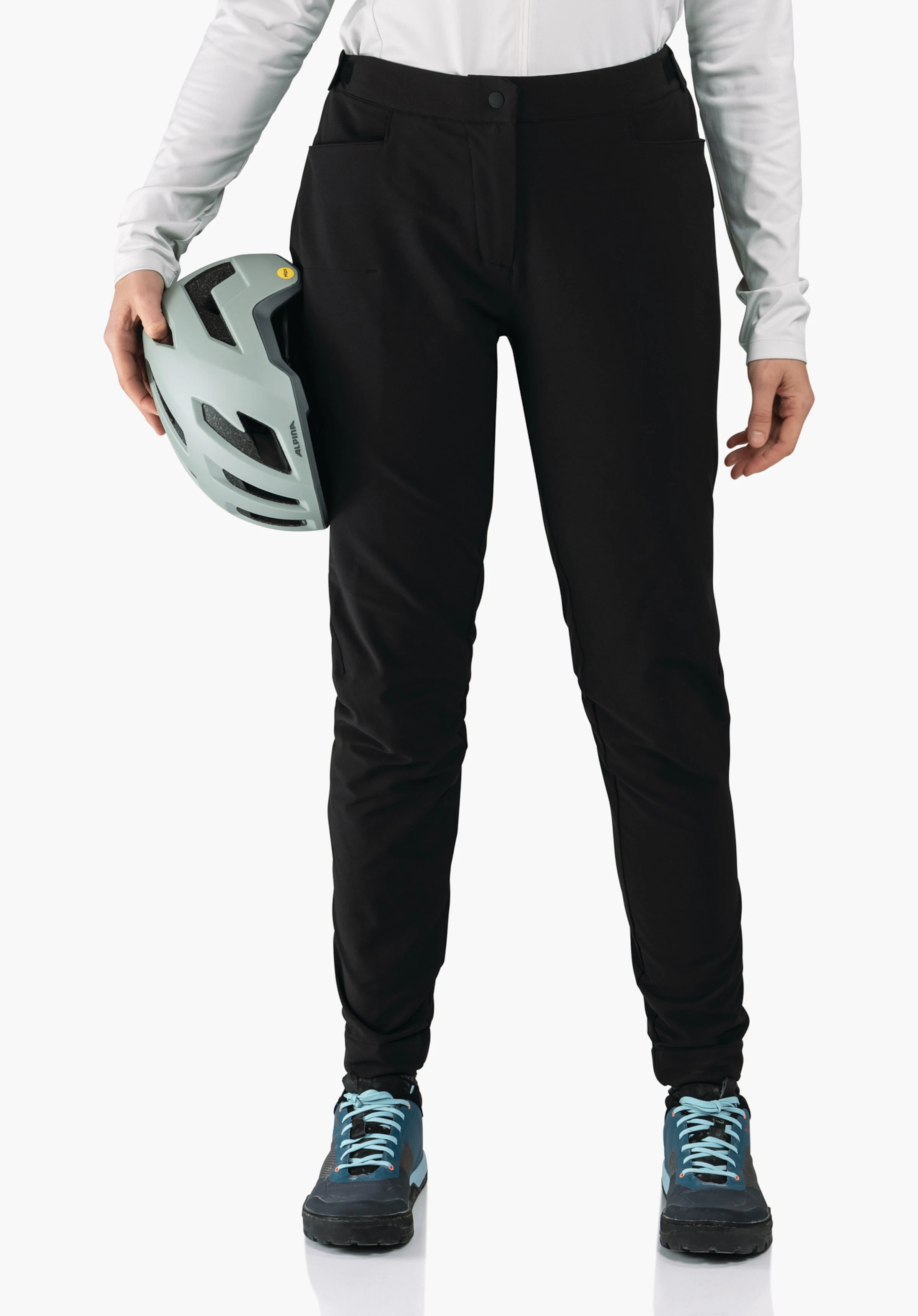 Pants Style Kubena WMS schwarze Hose; Person hält einen hellgrauen Fahrradhelm mit Schriftzug ALPINA, steht in weißem Langarmshirt und dunkelblauen Schuhen vor hellem einfarbigem Hintergrund.