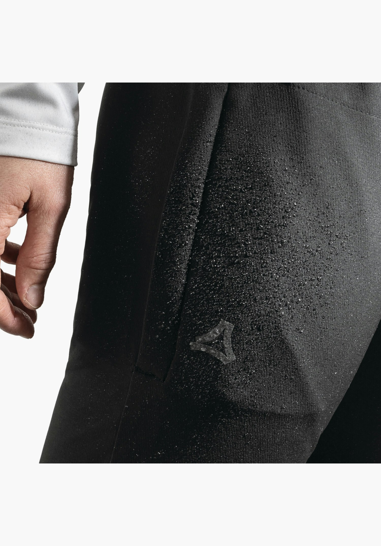 Pants Style Kubena WMS, de waterafstotende zwarte stof met waterdruppels en het Schöffel-logo als close-up voor een neutrale achtergrond.