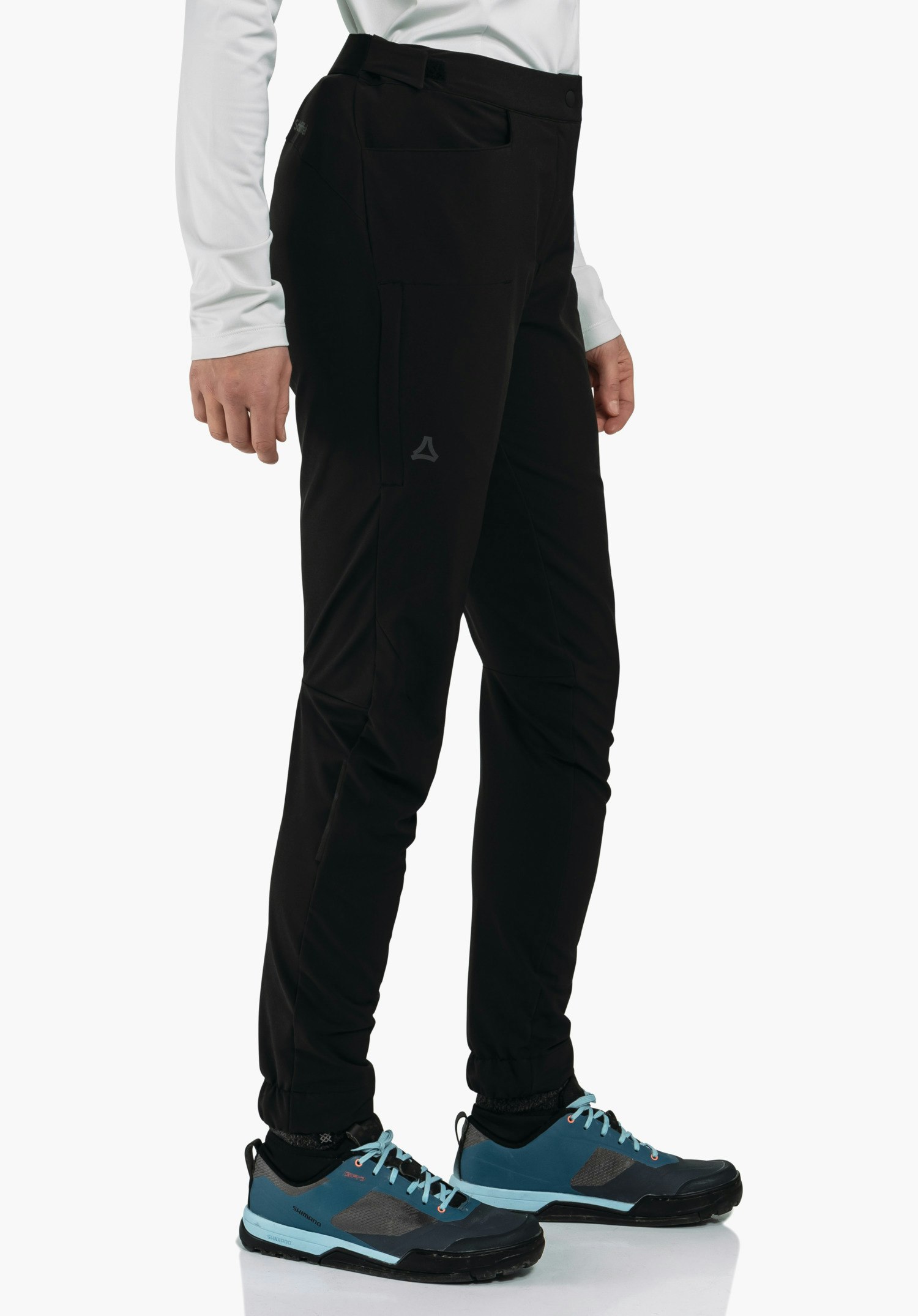 Pants Style Kubena WMS zwarte broek met Schöffel-logo, gedragen door een persoon; nauwsluitende pasvorm, gecombineerd met een wit bovenstuk en donkerblauwe wandelschoenen met lichtblauwe veters, voor een witte achtergrond.