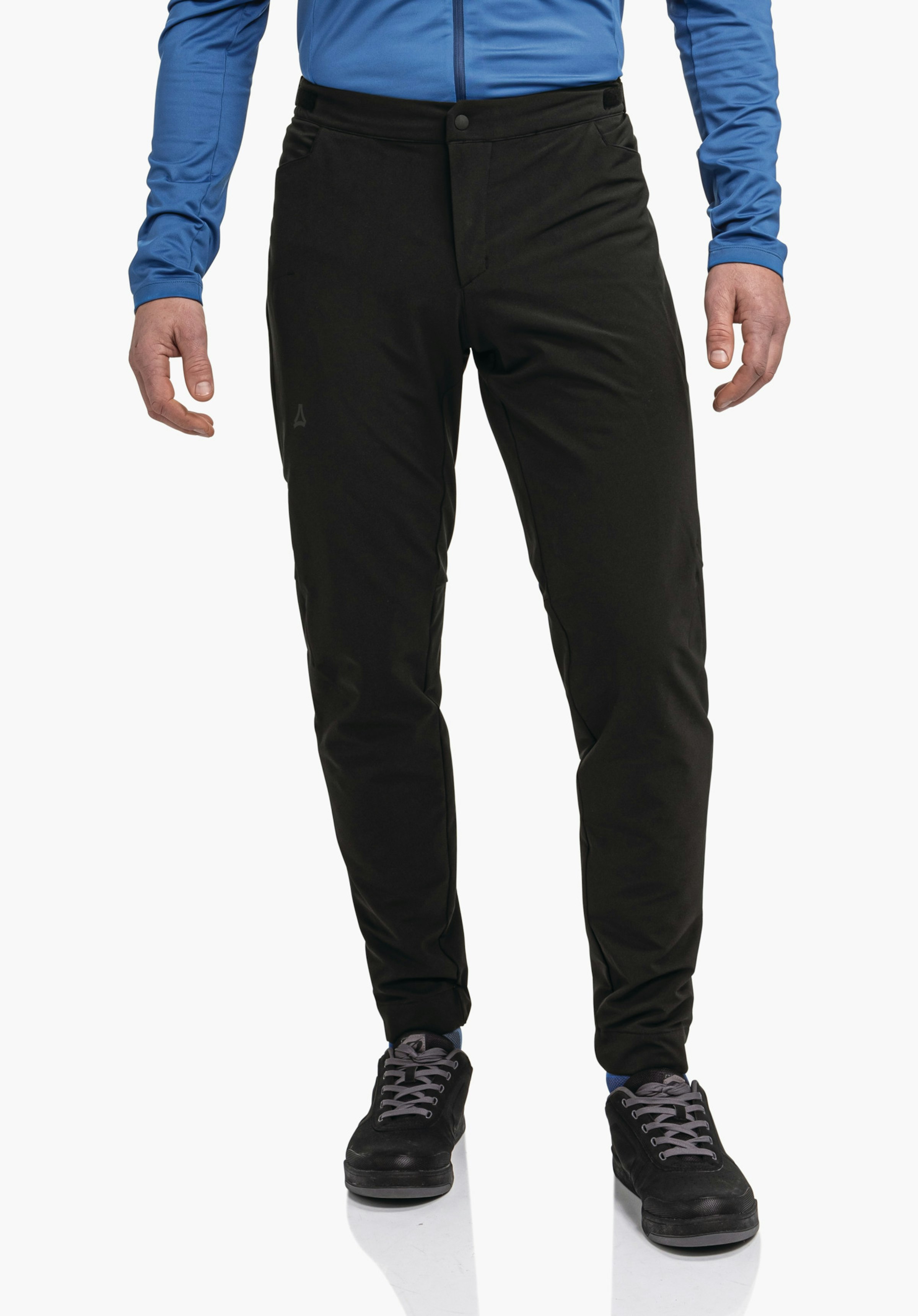 Pants Style Kubena MNS pantalon noir coupe ajustée, près du corps avec légers plis; logo Schöffel sur la cuisse gauche; porté par une personne avec un haut bleu clair et des chaussures noires devant un fond blanc.
