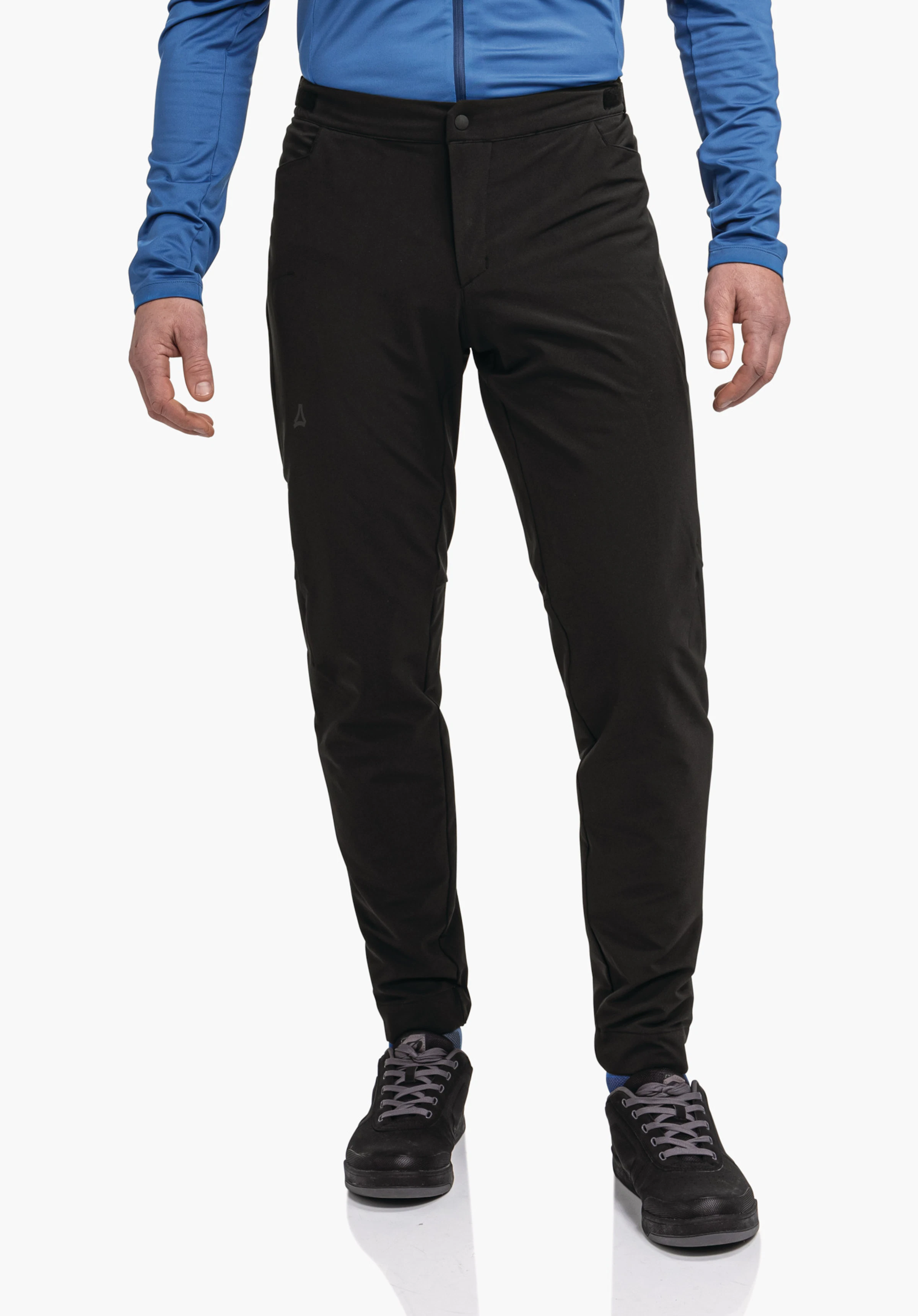 Pants Style Kubena MNS Schwarze, schmal geschnittene Hose, sitzt am Körper und zeigt leichte Falten; Schöffel-Logo an linker Oberschenkel; getragen von Person mit hellblauem Oberteil und schwarzen Schuhen vor weißem Hintergrund.
