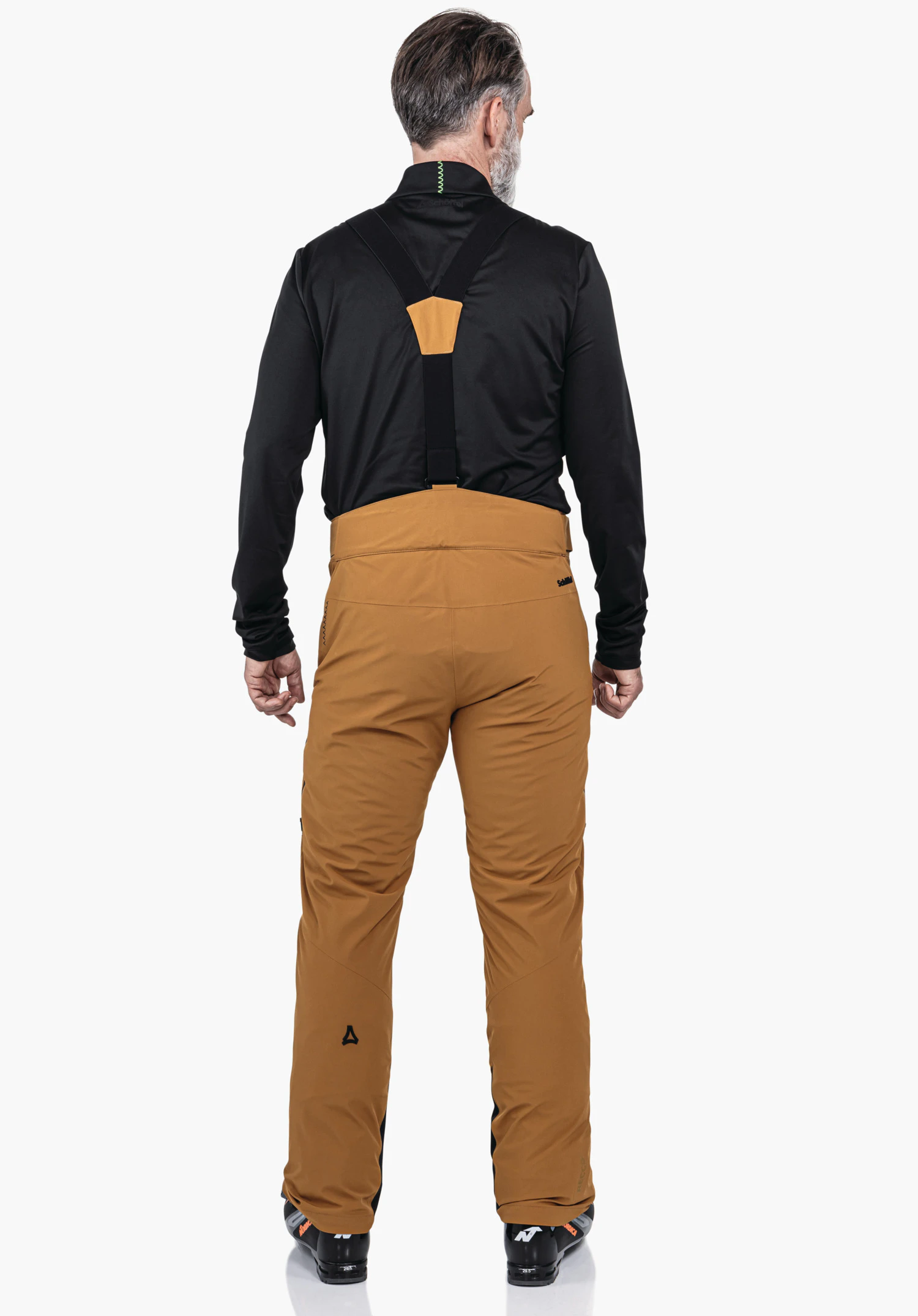 Pants Style Mountet MNS dark orange ski trousers worn by a man standing with black braces; black top; Schöffel logo on the lower leg; neutral white studio background.