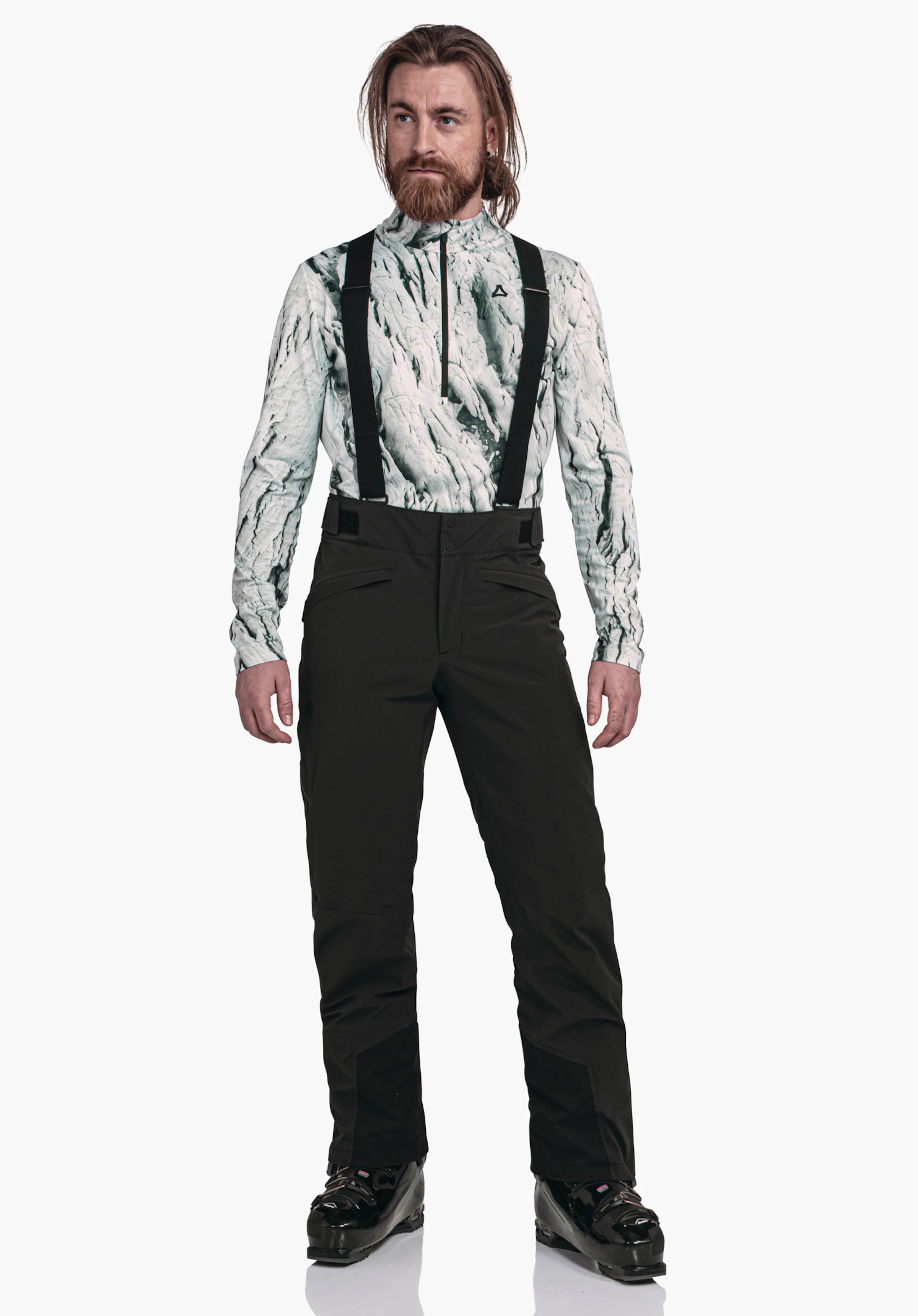 Pants Style Mountet MNS Mann trägt schwarze Skihose mit schwarzen Trägern, hellweißes Oberteil mit dunkelgrünem Muster, Schöffel-Logo auf der Brust, steht frontal vor hellweißem Hintergrund.