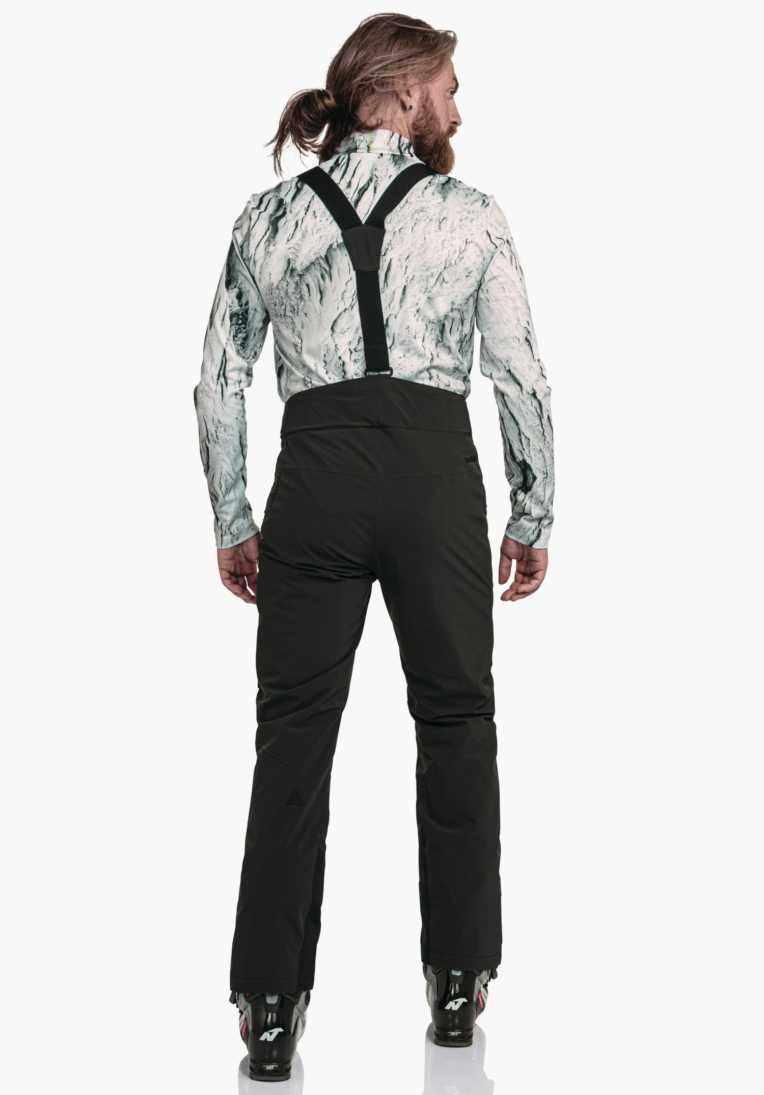 Pants Style Mountet MNS Schwarze Skihose mit schwarzen Hosenträgern, getragen von einer Person mit Rücken zur Kamera; weißes Oberteil mit dunkelgrünem Muster, Skischuhe sichtbar; Schöffel-Logo erkennbar.
