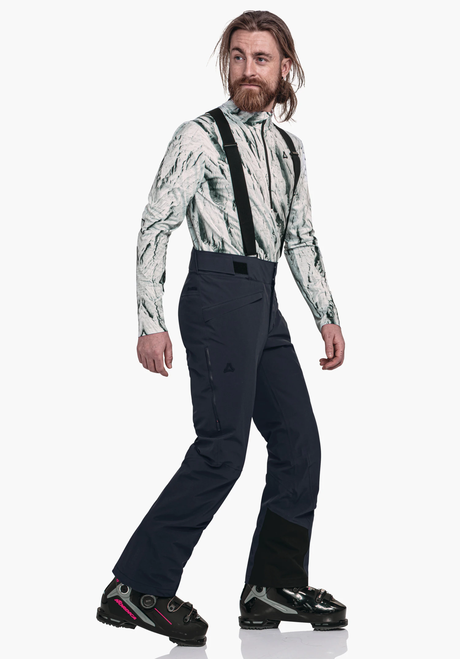 Pants Style Mountet MNS man in light white top with dark green pattern wears dark blue ski trousers with black braces; Schöffel logo visible; walks side-on in front of a white studio background, black ski boots with red details.