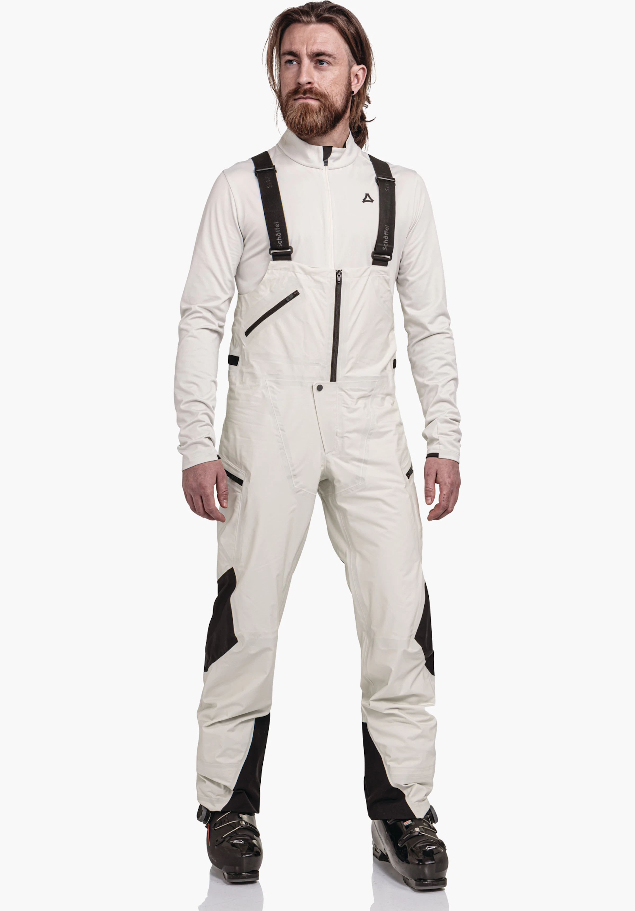 Pants Style Lufeld MNS salopette: man staat en draagt een lichtwitte salopette met zwarte applicaties en zwarte bretels; neutrale witte achtergrond. Schöffel-logo zichtbaar. Tekst op de bretels: "Schöffel".