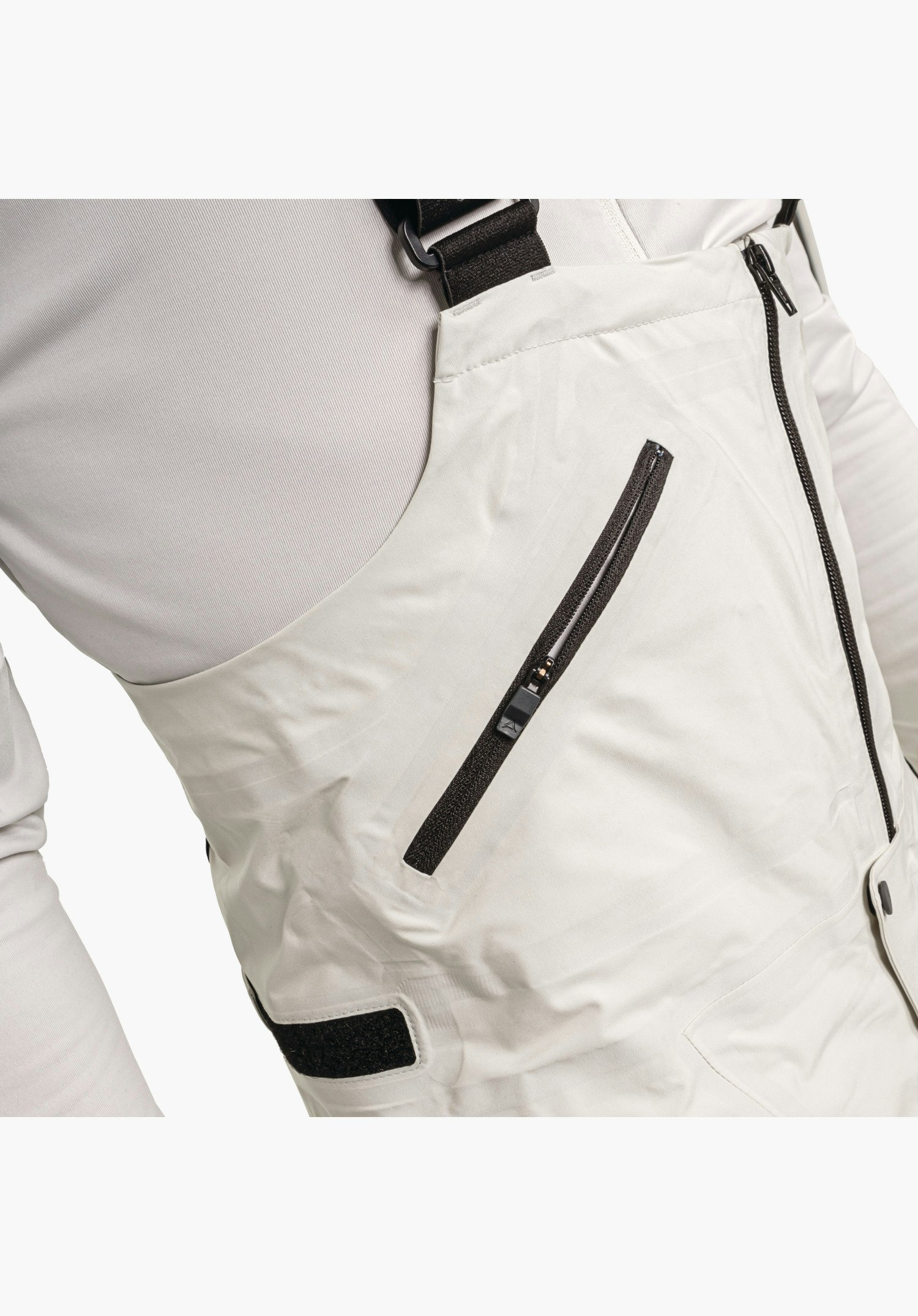 Pants Style Lufeld MNS detail view of the bib in nature colour featuring a diagonal zip pocket, adjustable strap and side fastening, close-up against a white/neutral background.