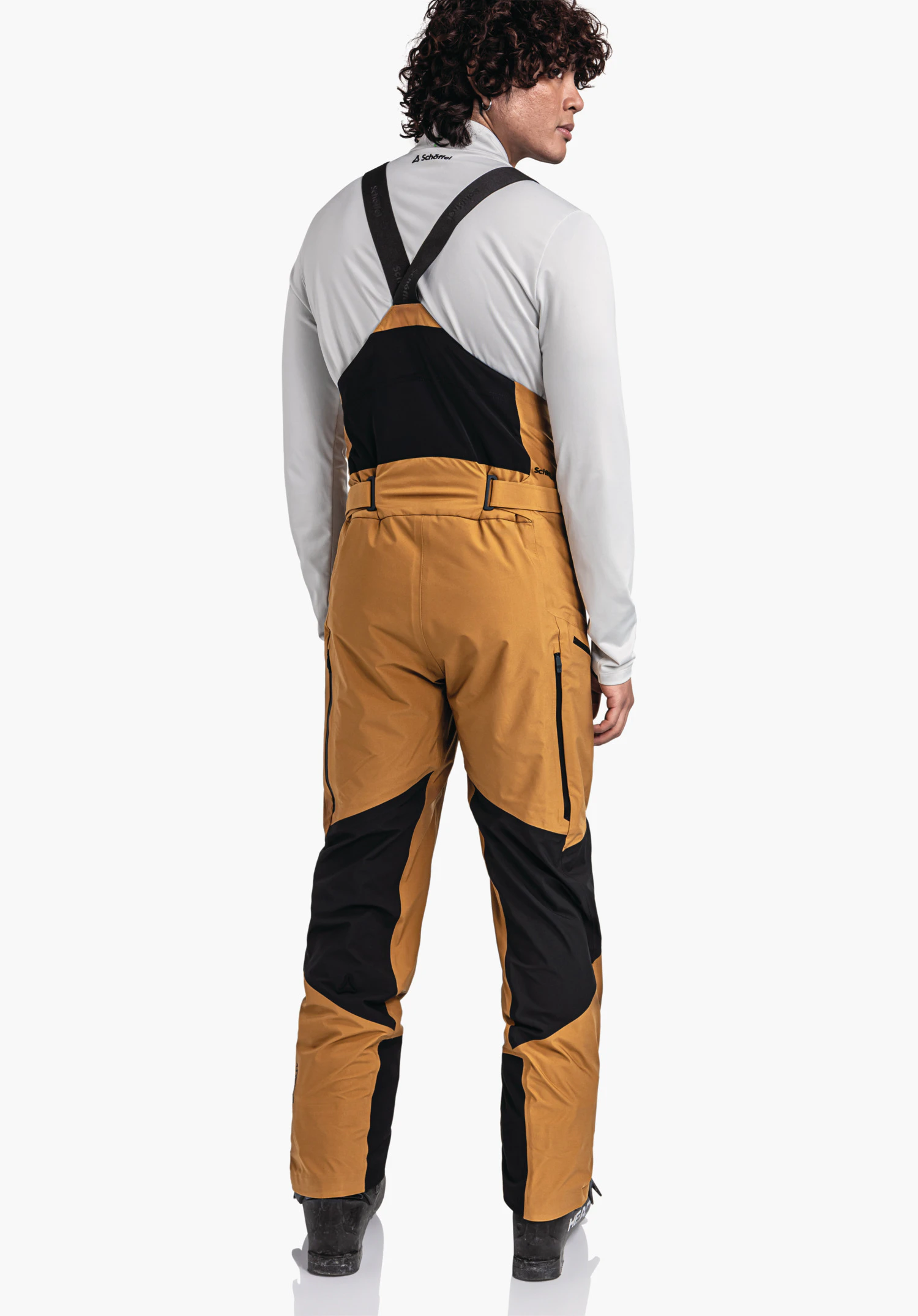 Pants Style Lufeld MNS Dunkel gelbe Skihose mit schwarzem Latz, Person steht aufrecht und blickt über die Schulter, vor weißem Hintergrund. Text: Schöffel-Logo, Schöffel, HEAD