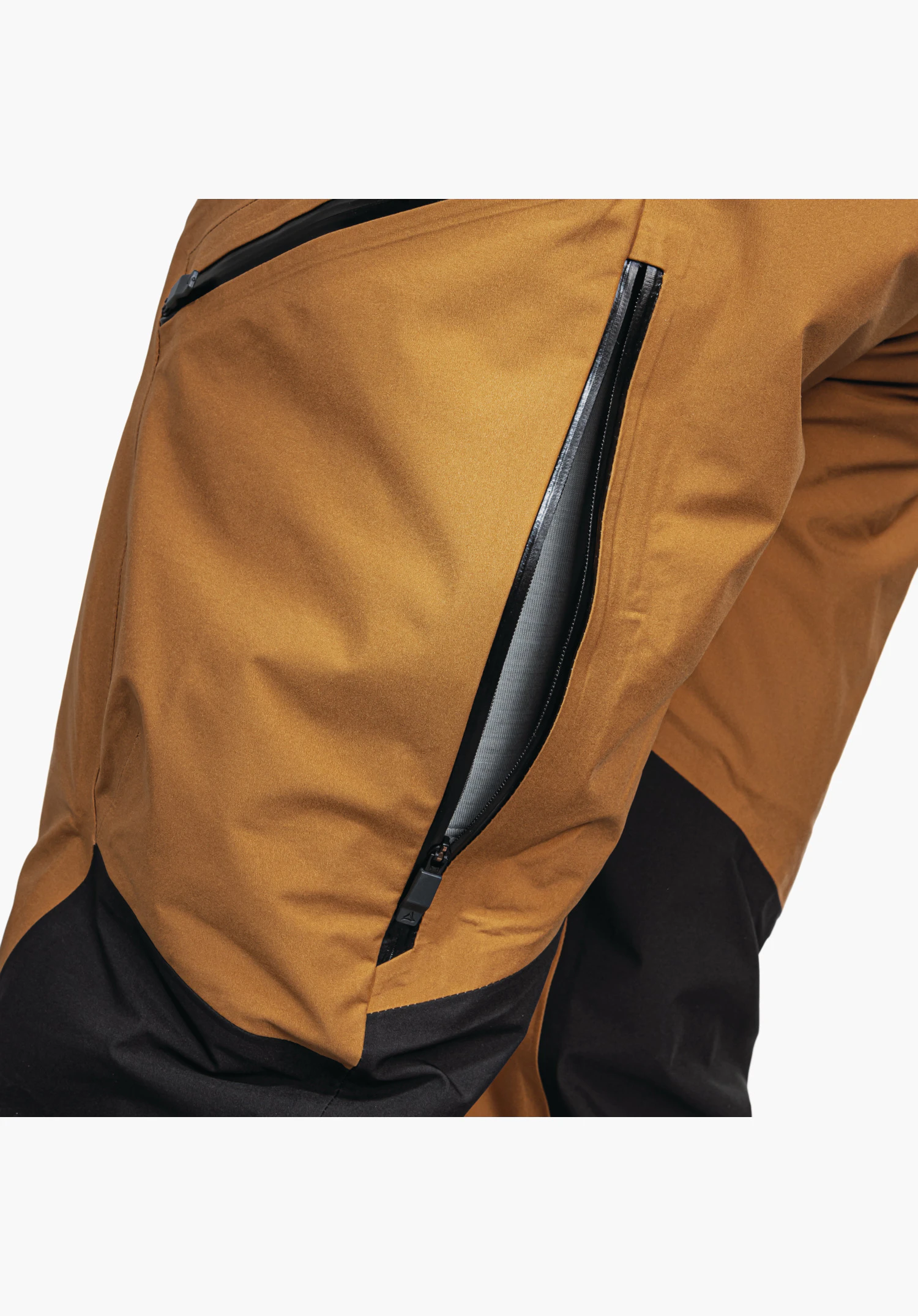 Pants Style Lufeld MNS zeigt den seitlichen, schwarzen Belüftungsreißverschluss auf dem braunen Oberschenkel. Detailaufnahme vor weißem Hintergrund.