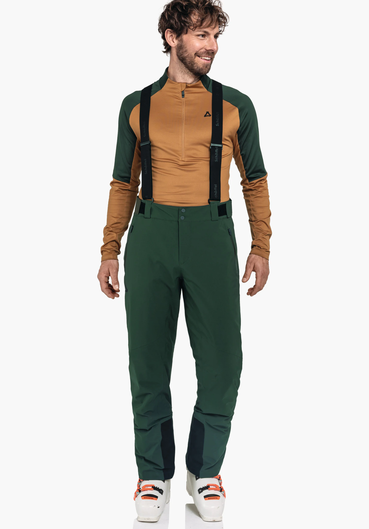 Pants Style Pine MNS homme portant un pantalon de ski vert foncé avec bretelles noires et un haut fonctionnel orange et vert foncé; logo Schöffel sur la poitrine; inscription sur les bretelles:"Schöffel"; debout devant un fond blanc.