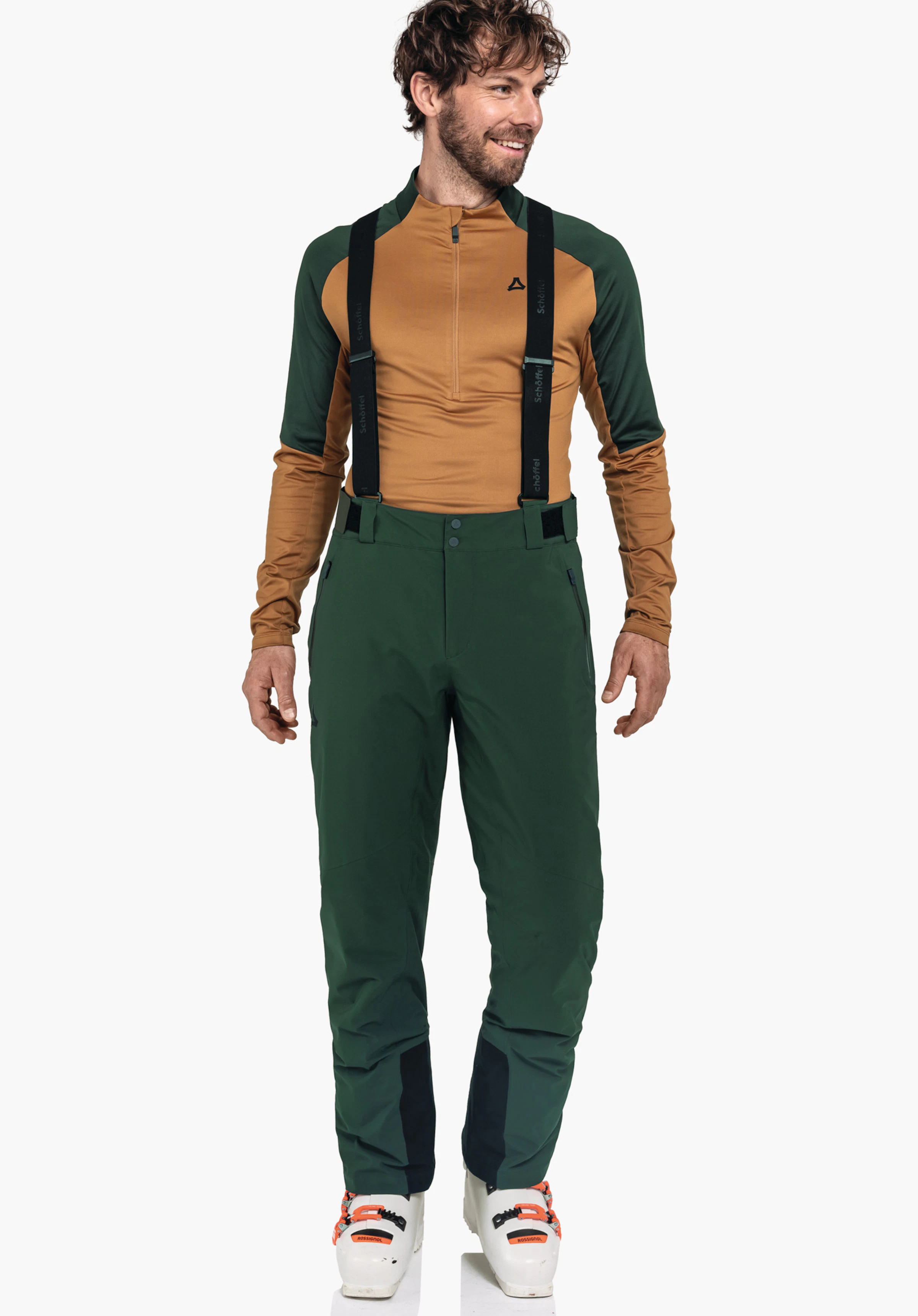Pants Style Pine MNS homme portant un pantalon de ski vert foncé avec bretelles noires et un haut fonctionnel orange et vert foncé; logo Schöffel sur la poitrine; inscription sur les bretelles:"Schöffel"; debout devant un fond blanc.