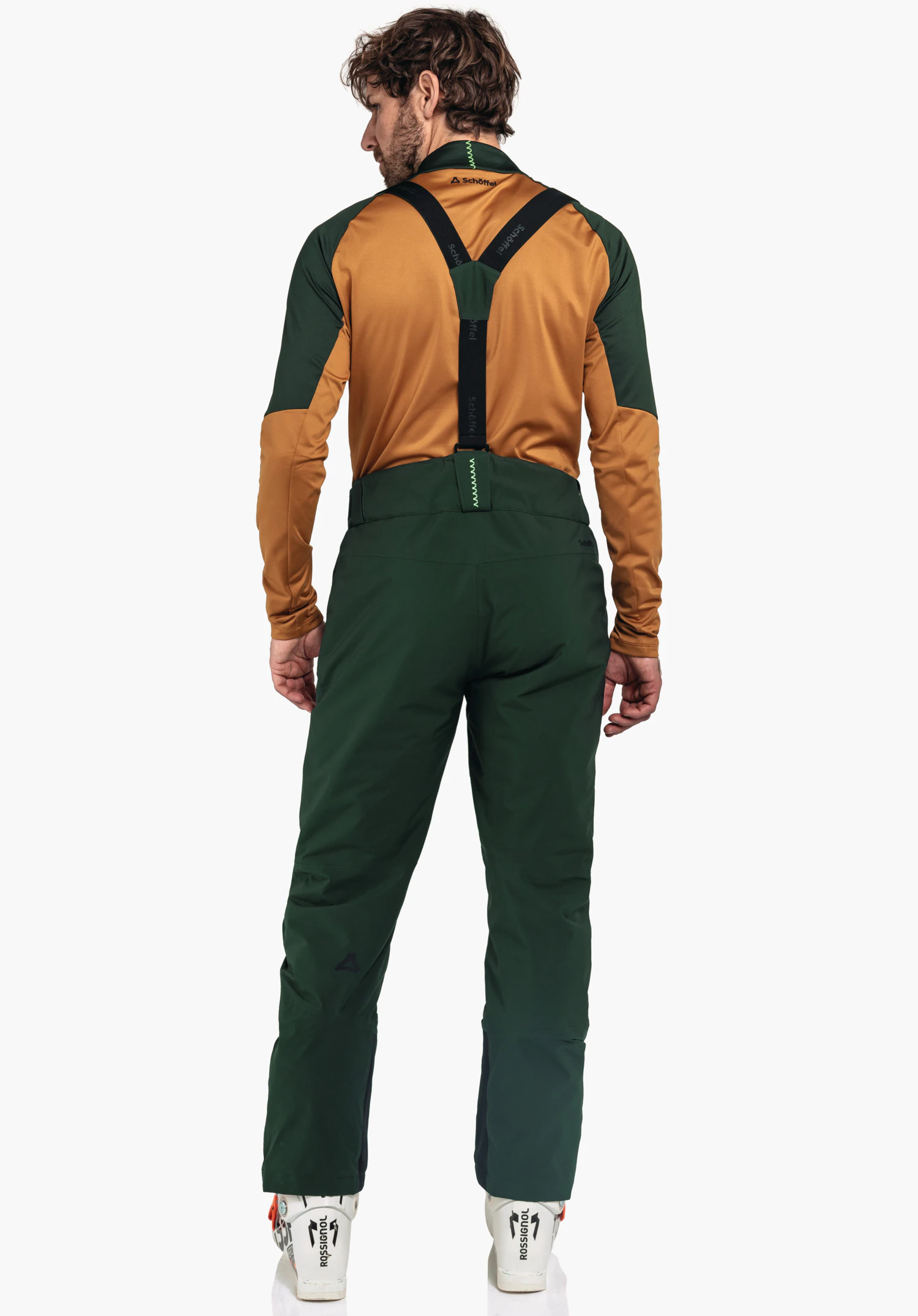 Pants Style Pine MNS homme portant un haut orange et un pantalon de ski vert foncé avec bretelles noires, debout dos à la caméra devant un fond blanc. Texte: "Schöffel", "schöffel", logo Schöffel, "ROSSIGNOL".