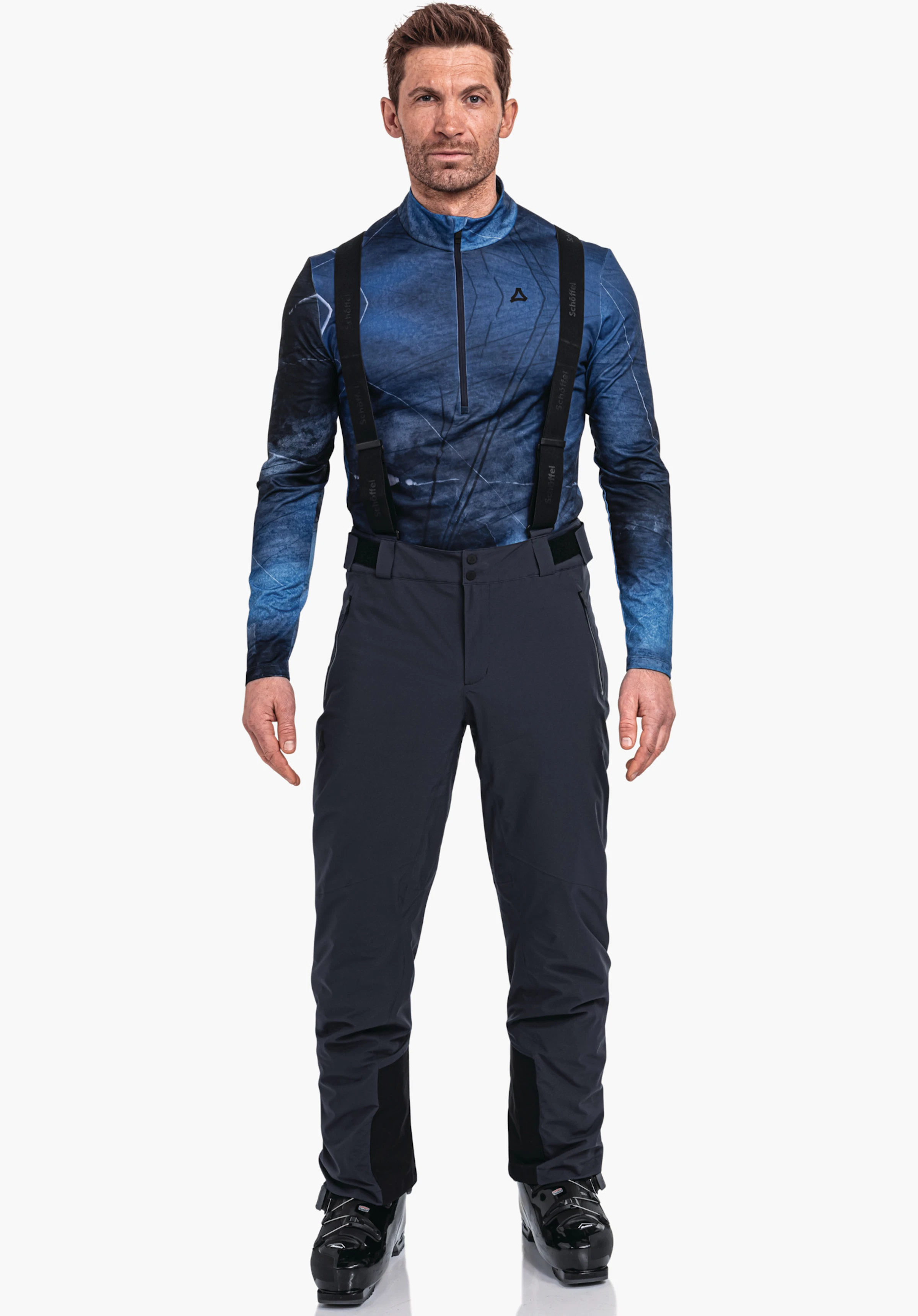Pants Style Pine MNS Mann trägt dunkelblaues Langarmshirt mit Schöffel-Logo, dunkelblaue Hose mit schwarzen Trägern, steht frontal, Arme locker, weißer Studiohintergrund. Text auf Trägern: "Schöffel".
