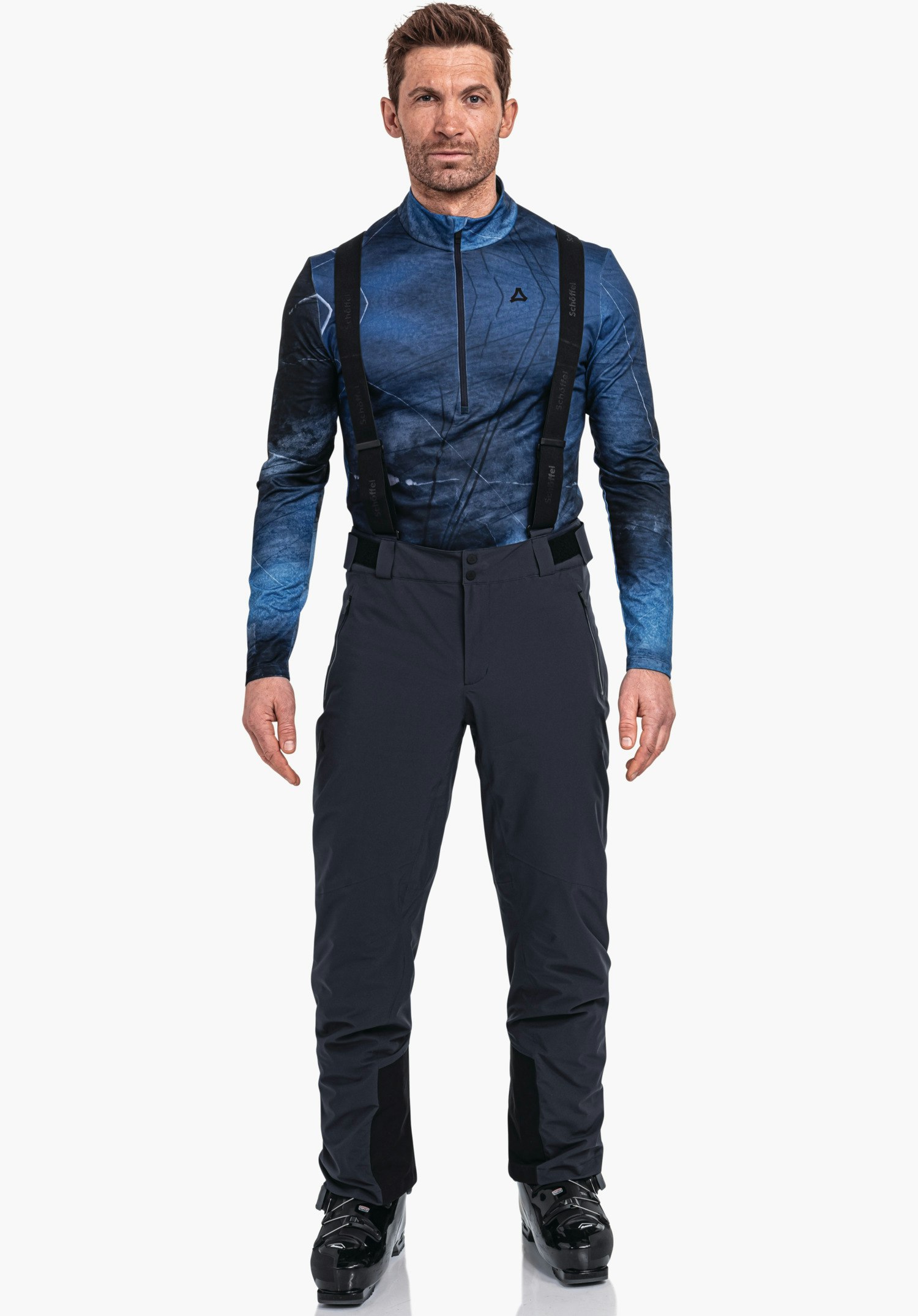 Pants Style Pine MNS Mann trägt dunkelblaues Langarmshirt mit Schöffel-Logo, dunkelblaue Hose mit schwarzen Trägern, steht frontal, Arme locker, weißer Studiohintergrund. Text auf Trägern: "Schöffel".