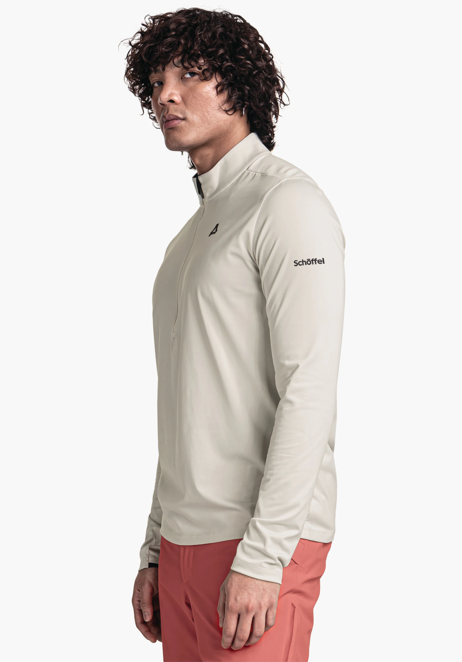 Longsleeve Style Pine MNS veste manches longues gris clair avec logo Schöffel sur la poitrine, portée par une personne debout de profil, regard vers l’avant; texte sur la manche: "Schöffel". Pantalon rouge, fond clair neutre.