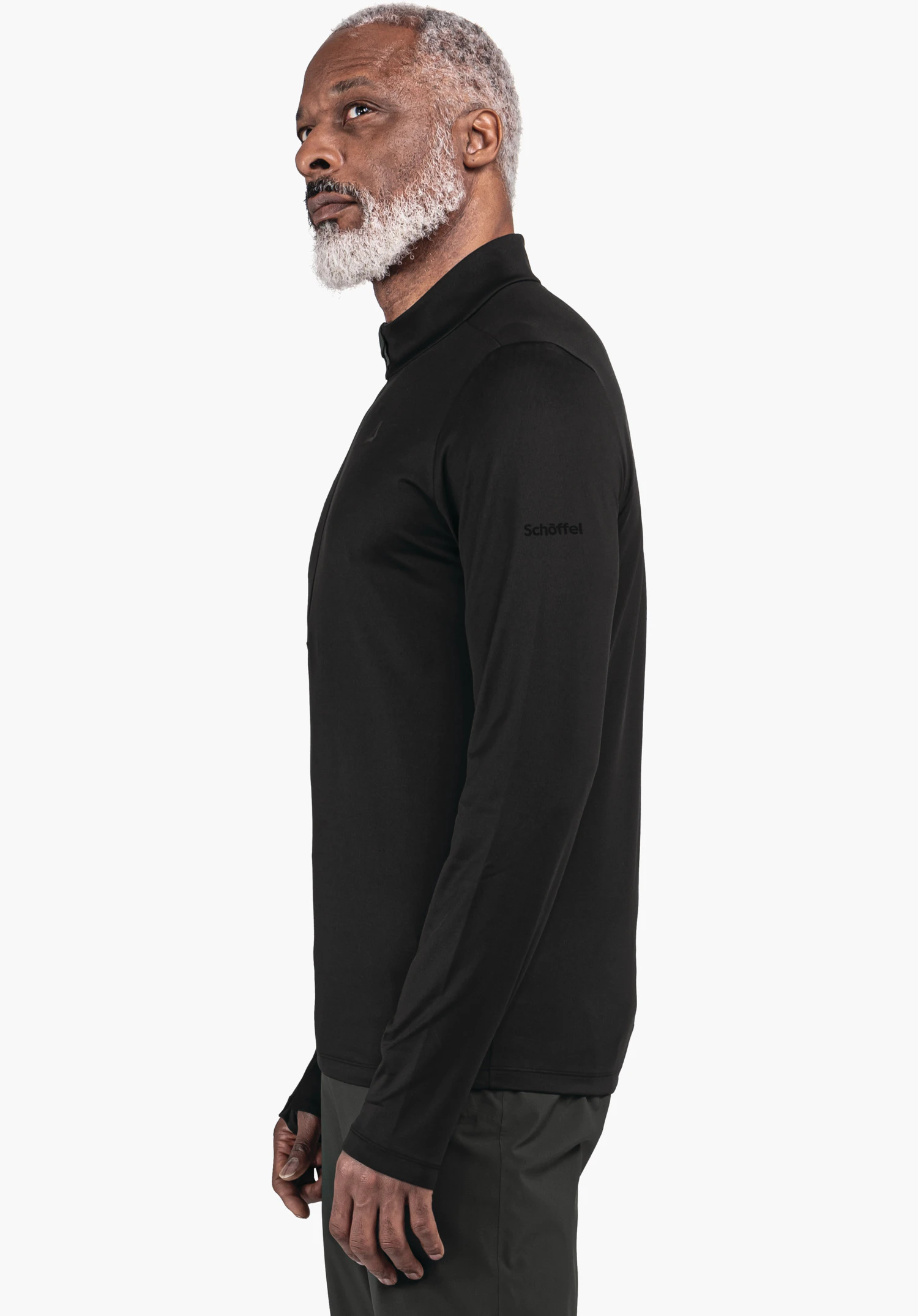 Longsleeve Style Pine MNS Mann in schwarzem Langarmshirt steht seitlich und blickt nach oben-links vor weißem Hintergrund. Auf dem linken Ärmel steht „Schöffel“.