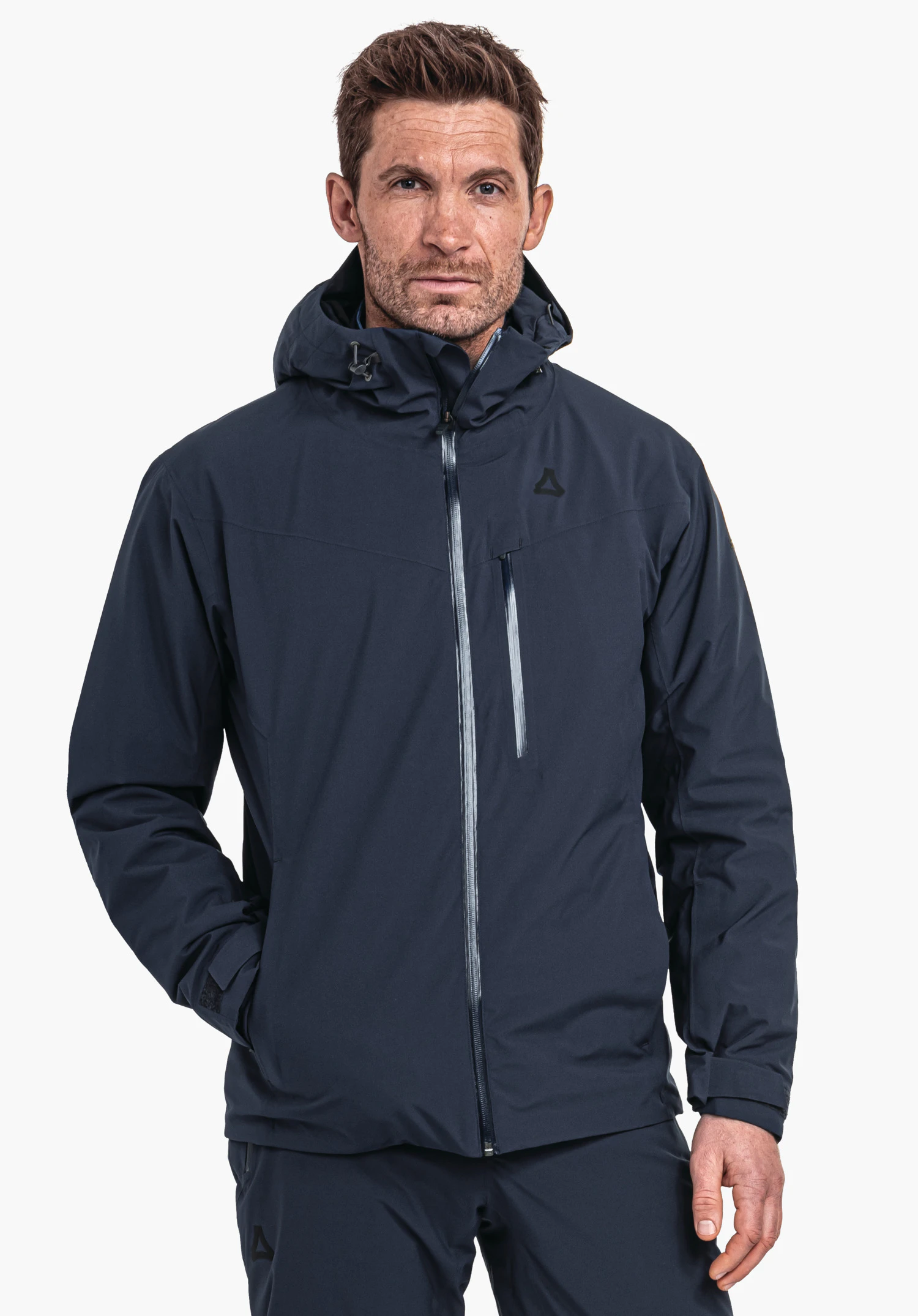 Jacket Style Nollen MNS homme portant un parka bleu foncé, debout de face, main droite dans la poche, bras gauche détendu; logo Schöffel sur la poitrine gauche; fond clair neutre.