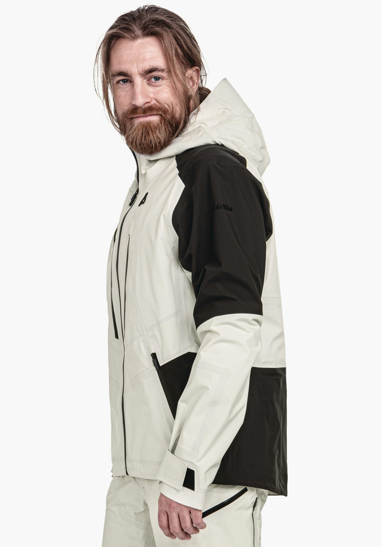 Shell Jk Style Lufeld MNS off-white and dark green outdoor jacket, worn sideways by a bearded man with a slight smile; Schöffel logo visible. Text: "Schöffel". Neutral white background.