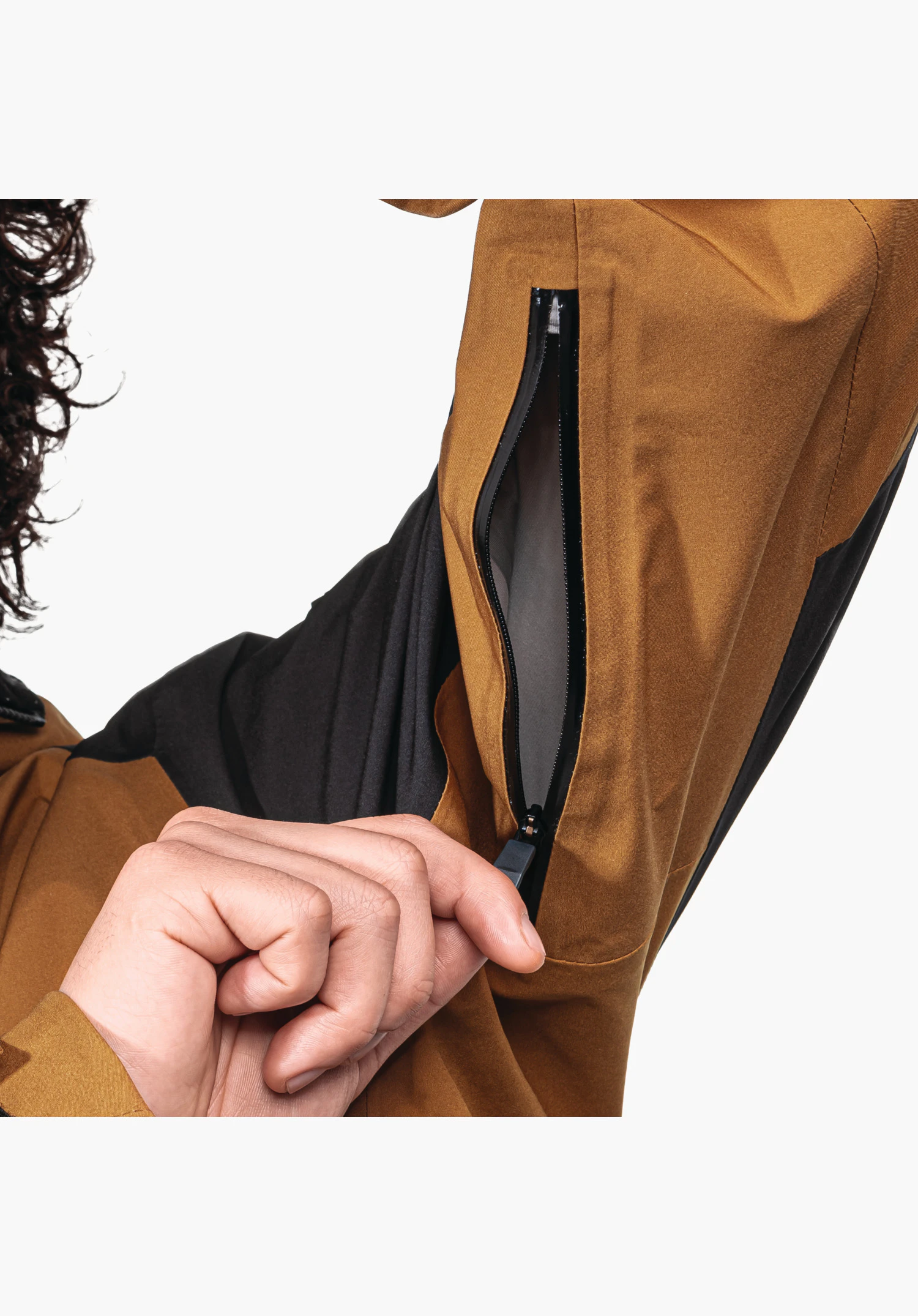 Shell Jk Style Lufeld MNS zeigt den geöffneten Reißverschluss zur Unterarmbelüftung im braunen Material, wobei eine Hand den Zipper bedient, Nahaufnahme vor weißem Hintergrund.