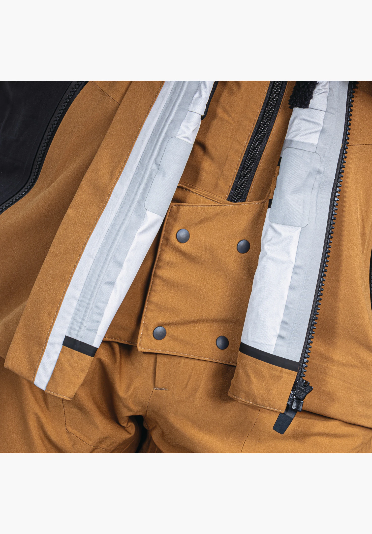 Shell Jk Style Lufeld MNS. Detailaufnahme der inneren Sturmleiste und des Reißverschlusses mit Druckknöpfen am braunen Stoff. Nahaufnahme vor weißem/neutralem Hintergrund.