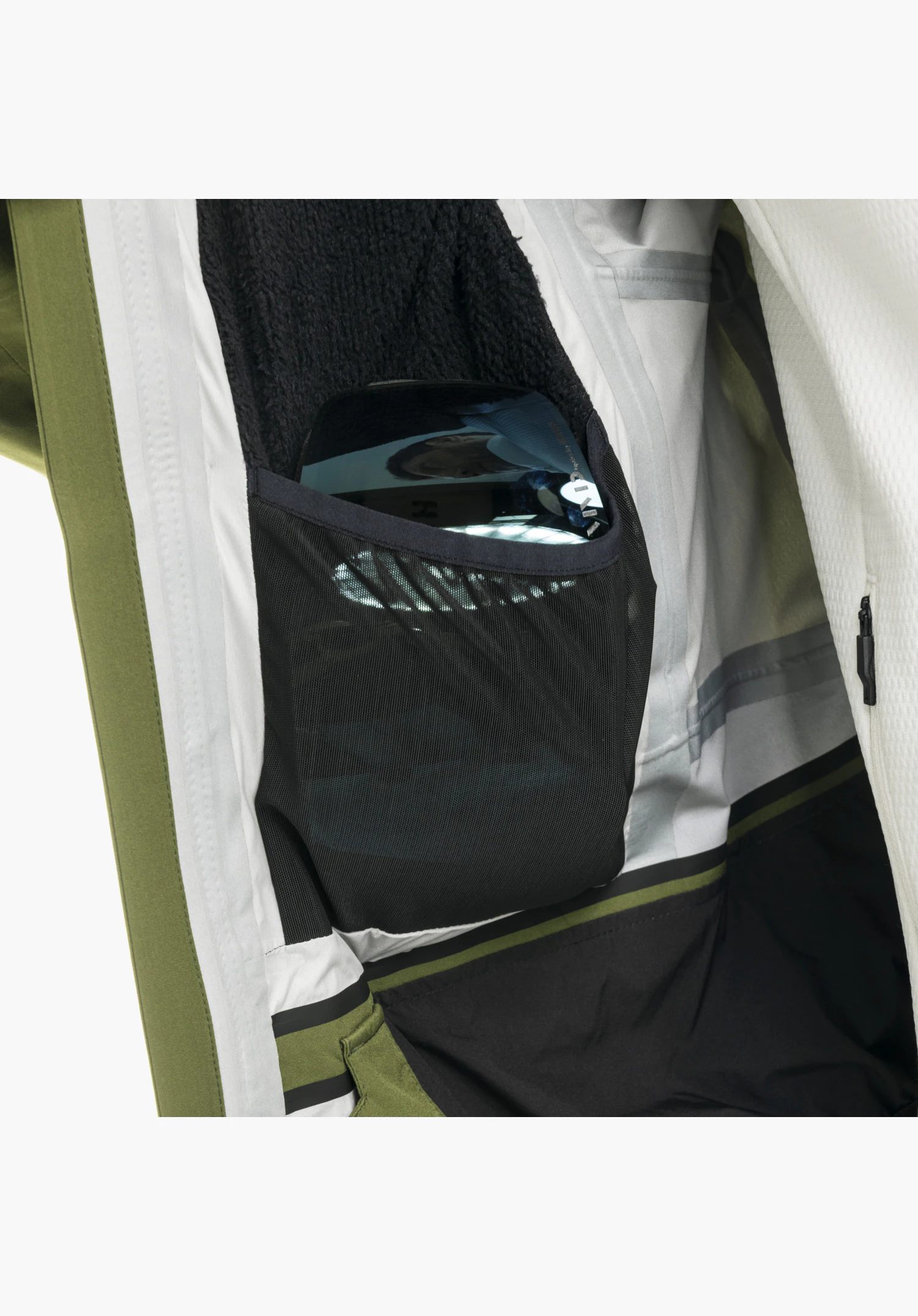 Shell Jk Style Lufeld MNS Innentasche aus schwarzem Mesh-Gewebe mit einer Skibrille darin in der grünen Jacke, Nahaufnahme vor neutralem Hintergrund.
