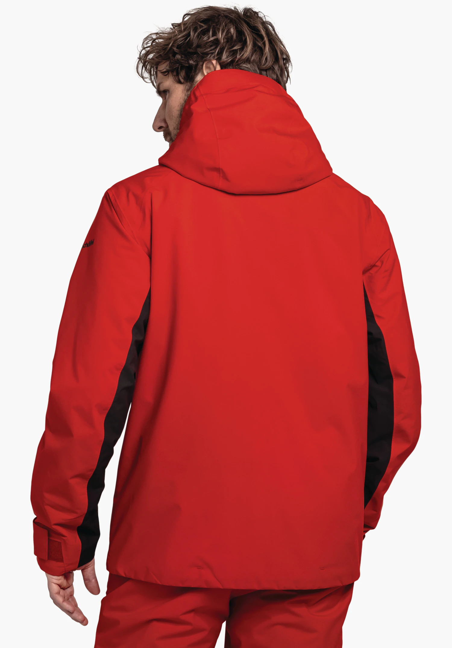 Jacket Style Trifex MNS rode jas; persoon staat met de rug naar de camera en kijkt naar links, zwarte zijpanelen, capuchon, rood broekspijp zichtbaar, witte studioachtergrond.