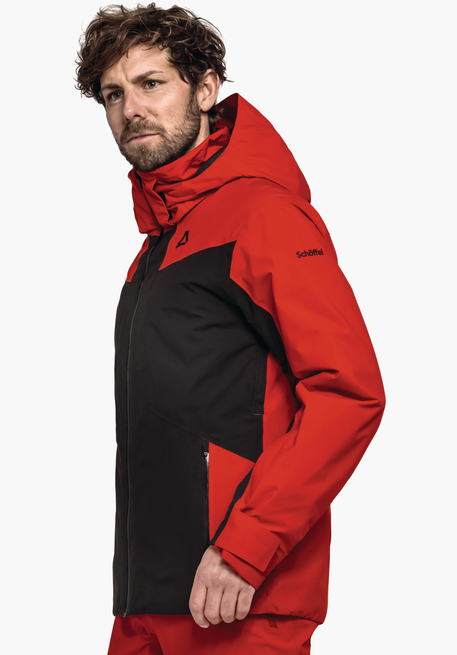 Jacket Style Trifex MNS man draagt een rood-zwarte jas met Schöffel-logo en tekst "Schöffel", kijkt zijwaarts en staat voor een witte achtergrond.