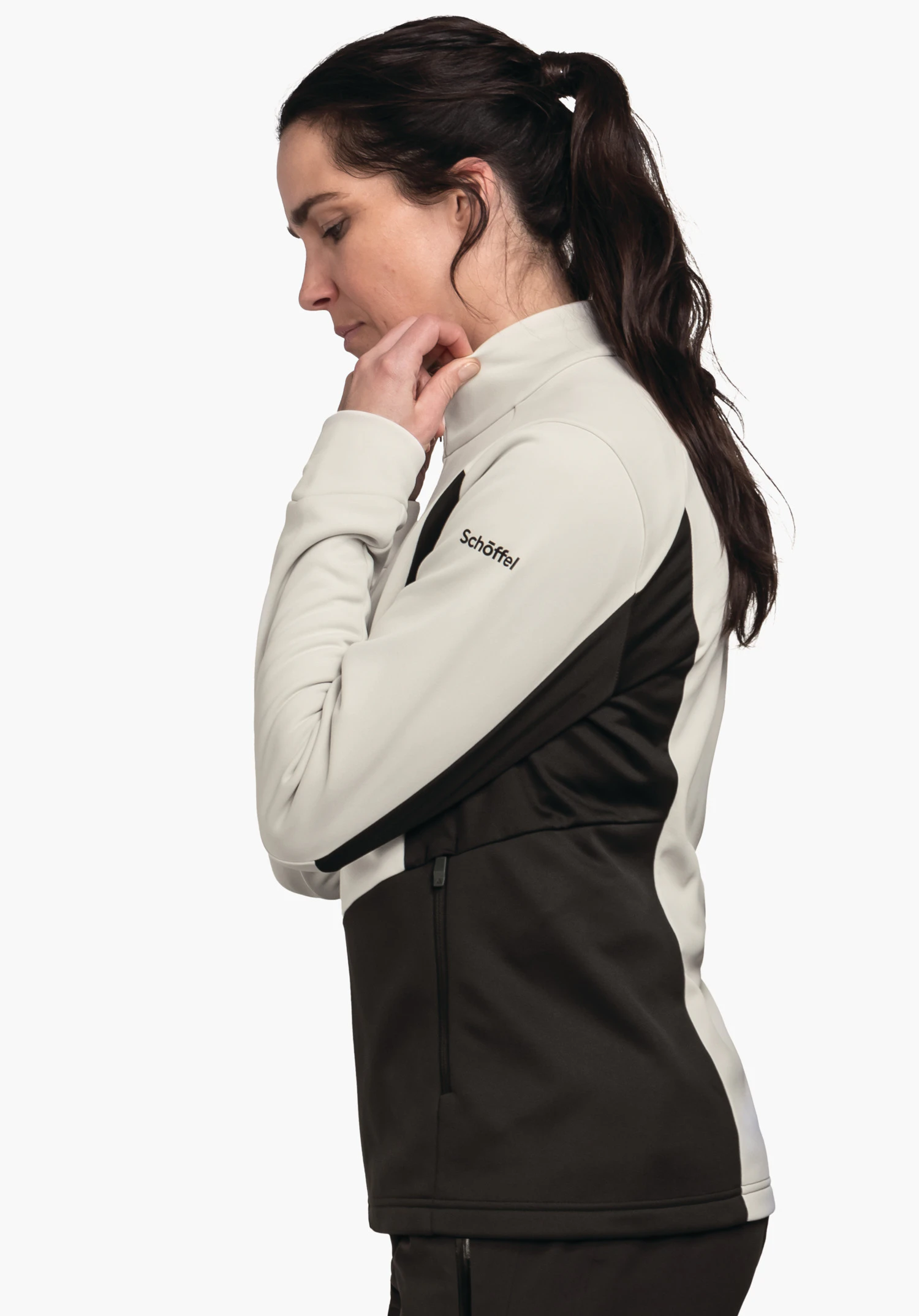 Fleece Jk Style Pontre WMS Frau in hellweiß und schwarz Jacke, sie fasst den Kragen, blickt seitlich nach unten, neutraler weißer Hintergrund. Text auf Ärmel: "Schöffel".