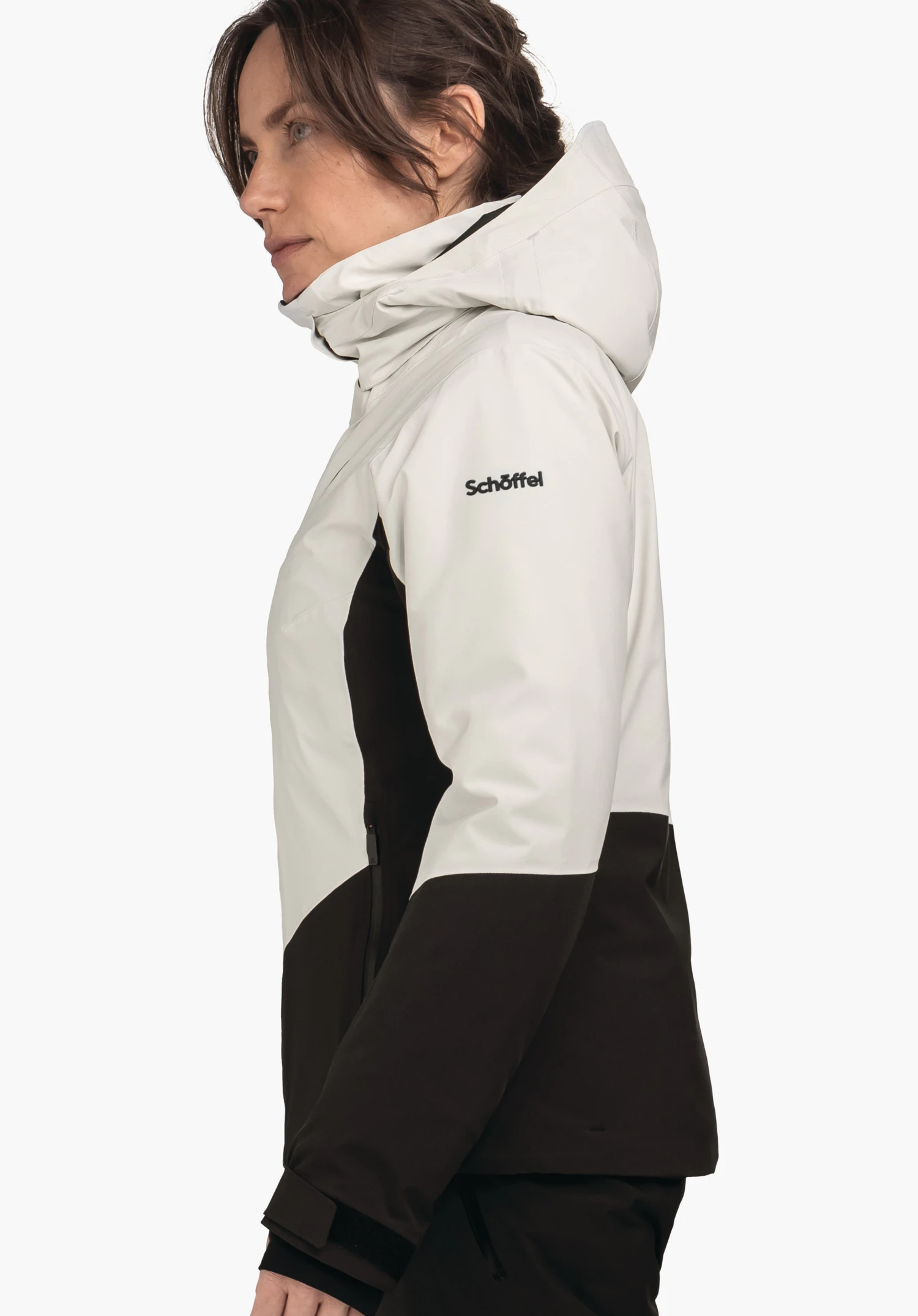 Jacket Style Safuna WMS jas in lichtwit boven en zwart onder; vrouw draagt deze zijwaarts met opgezette capuchon en ontspannen arm. Tekst op de mouw: "Schöffel".