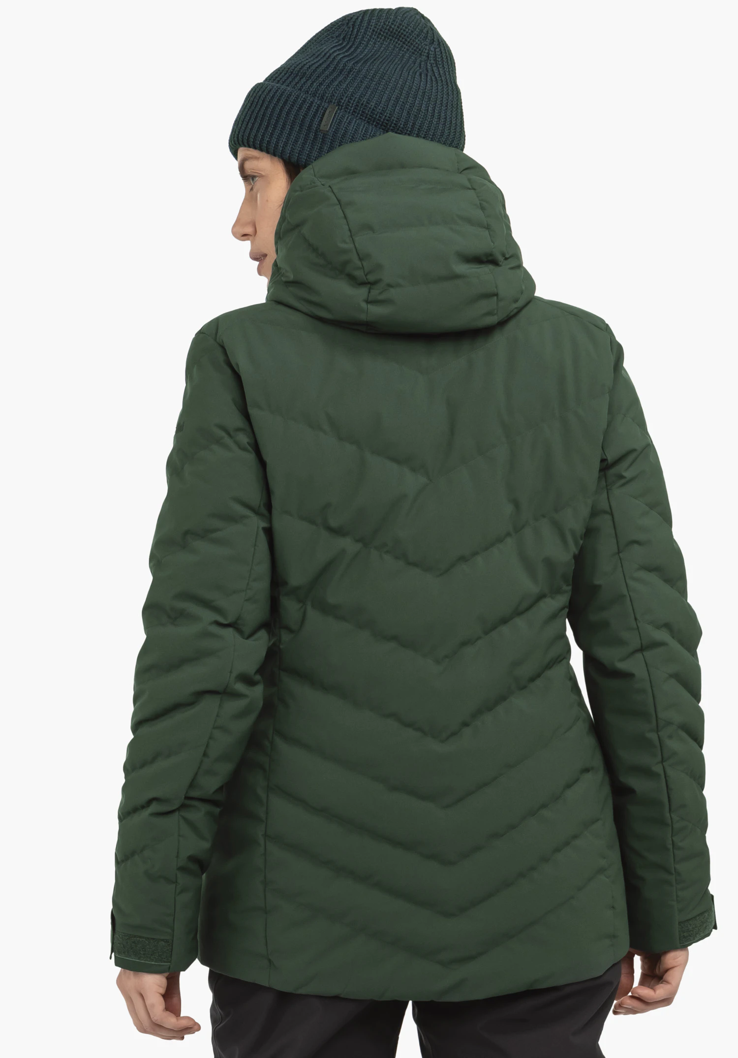 Jacket Style Alerce WMS donkergroene gewatteerde jas met capuchon, van achteren gedragen; jas met V-vormige stiknaden, gecombineerd met een donkergroene gebreide muts, neutrale lichte achtergrond.