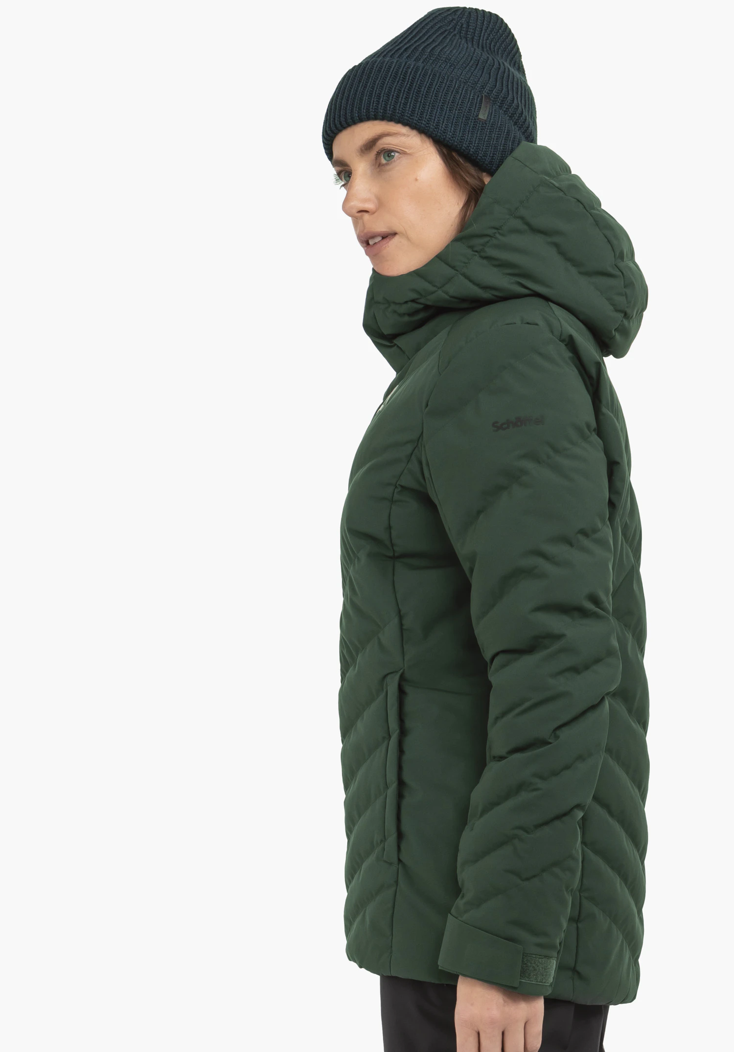 Jacket Style Alerce WMS donkergroene doorgestikte jas met capuchon, gedragen door een persoon in profiel naar rechts; donkerblauwe gebreide muts; egale witte achtergrond. Tekst op de mouw: Schöffel.