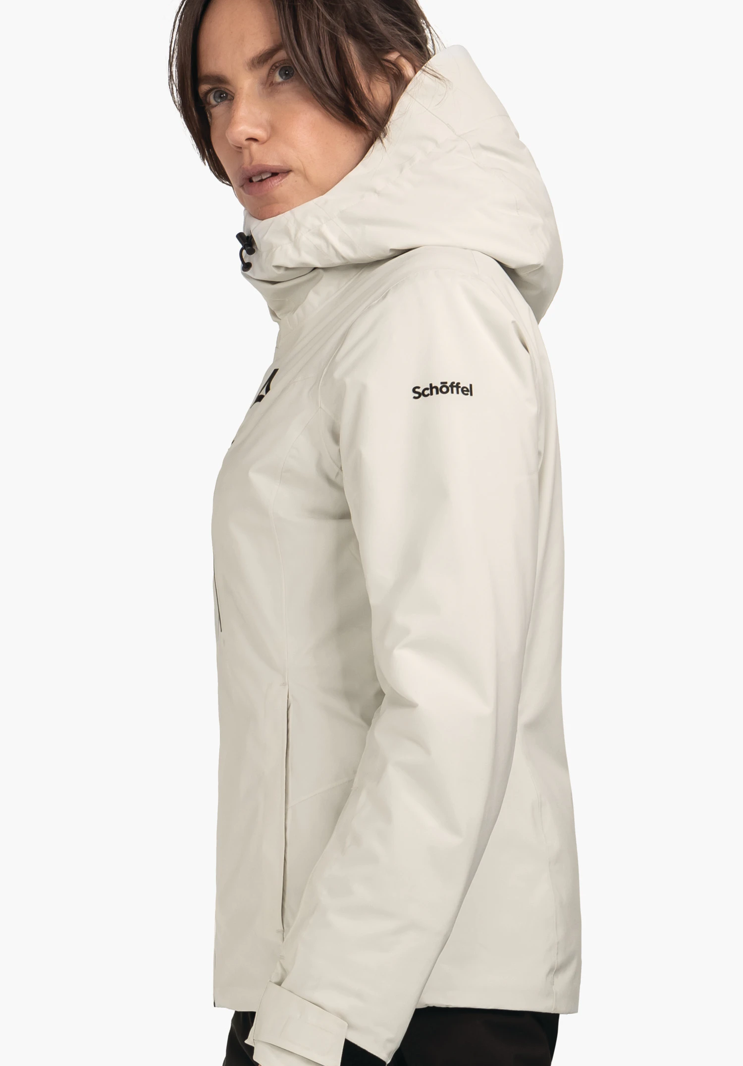 Jacket Style Nollen WMS jas gedragen door een vrouw die zijwaarts staat en naar rechts kijkt; lichtwitte jas met Schöffel-logo op de borst en tekst "Schöffel" op de mouw; witte achtergrond.