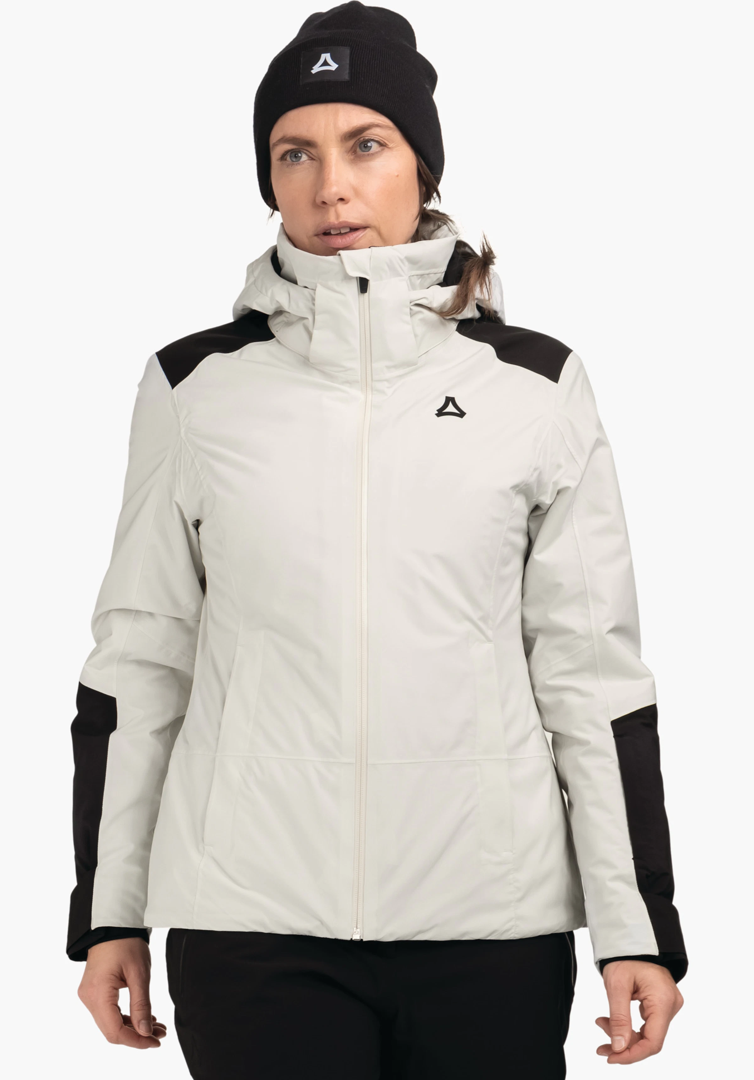 Jacket Style Zandwel WMS veste de ski blanc clair avec empiècements noirs, portée par une femme; logo Schöffel sur la poitrine et le bonnet, debout de face devant un fond studio clair neutre.