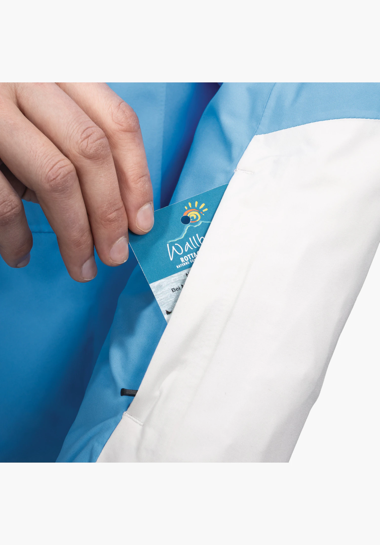 Jacket Style Zandwel WMS montre la poche pratique pour forfait de ski sur la manche en détail. Une main glisse une carte dans le compartiment du modèle bleu avec un accent blanc. Gros plan sur fond blanc/neutre.