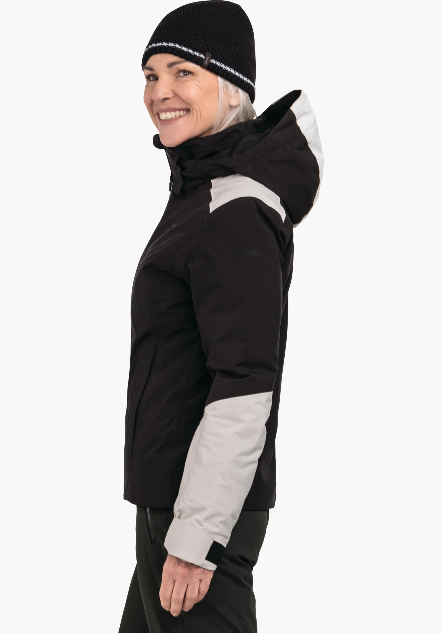 Jacket Style Trifex WMS femme souriante; porte une veste de ski à capuche rouge et bleu foncé, pose de profil devant fond blanc. Visible: logo Schöffel sur la poitrine, inscription "schöffel" sur la manche.