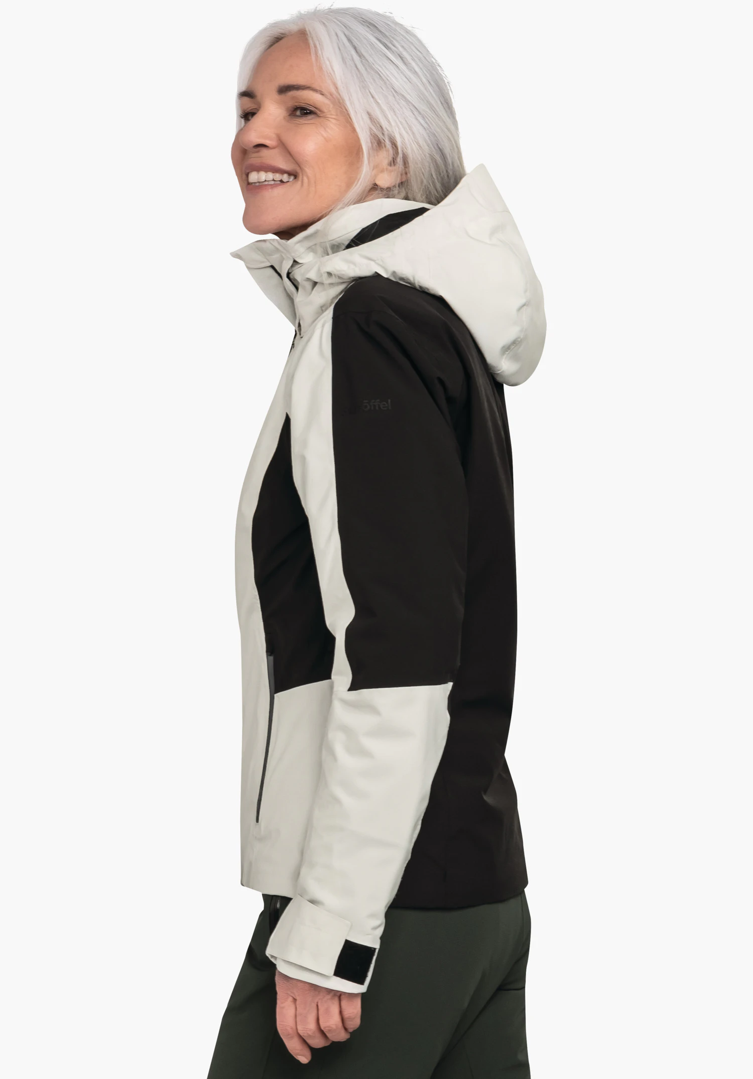 Jacket Style Trifex WMS outdoorjas: vrouw met licht wit haar draagt een wit-zwart jas, glimlacht zijwaarts voor een witte achtergrond. Tekst op de mouw: "Schöffel".