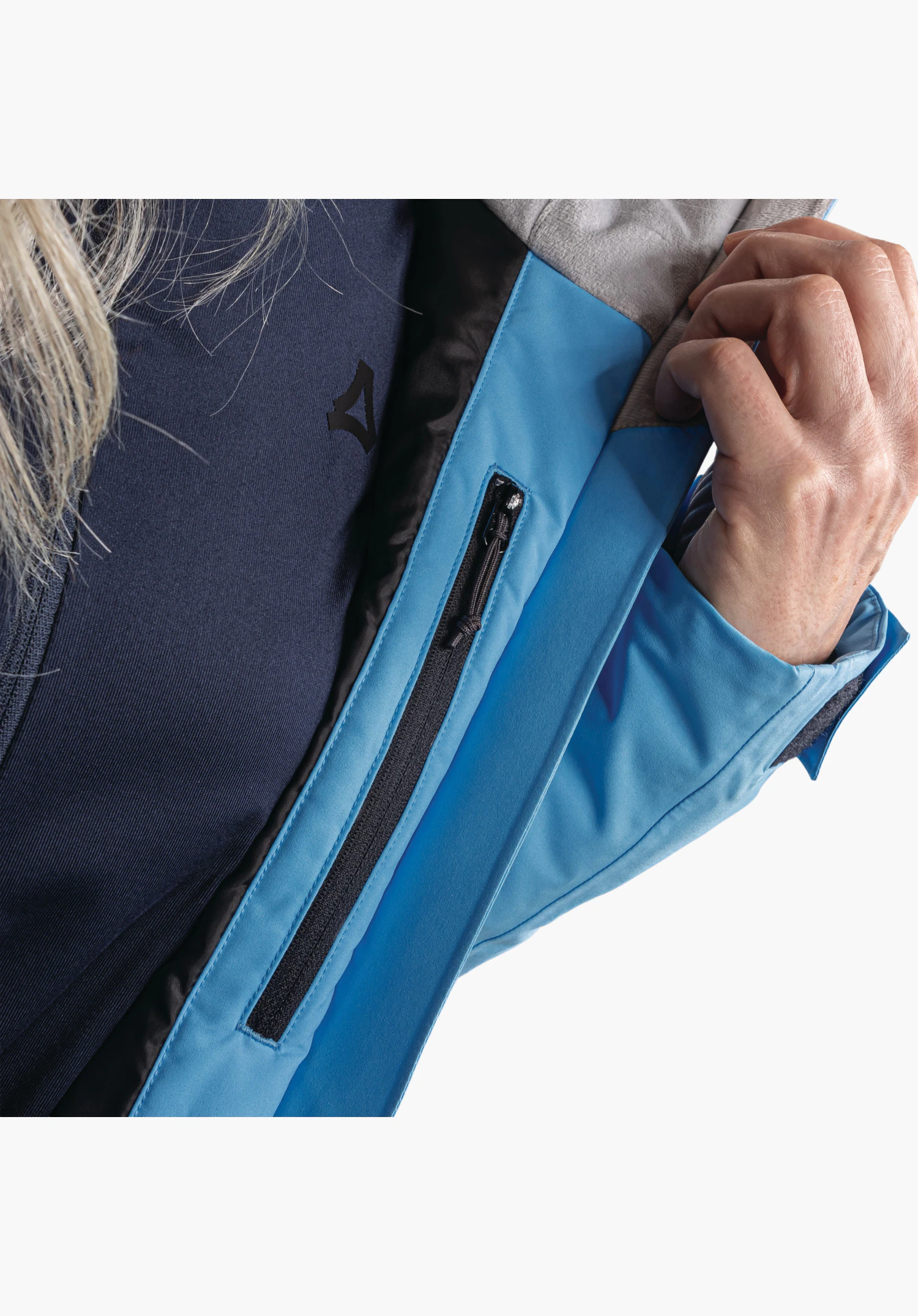 Jacket Style Trifex WMS, vue détaillée de la poche zippée verticale dans le tissu bleu révélée par une main, gros plan sur fond blanc/neutre.