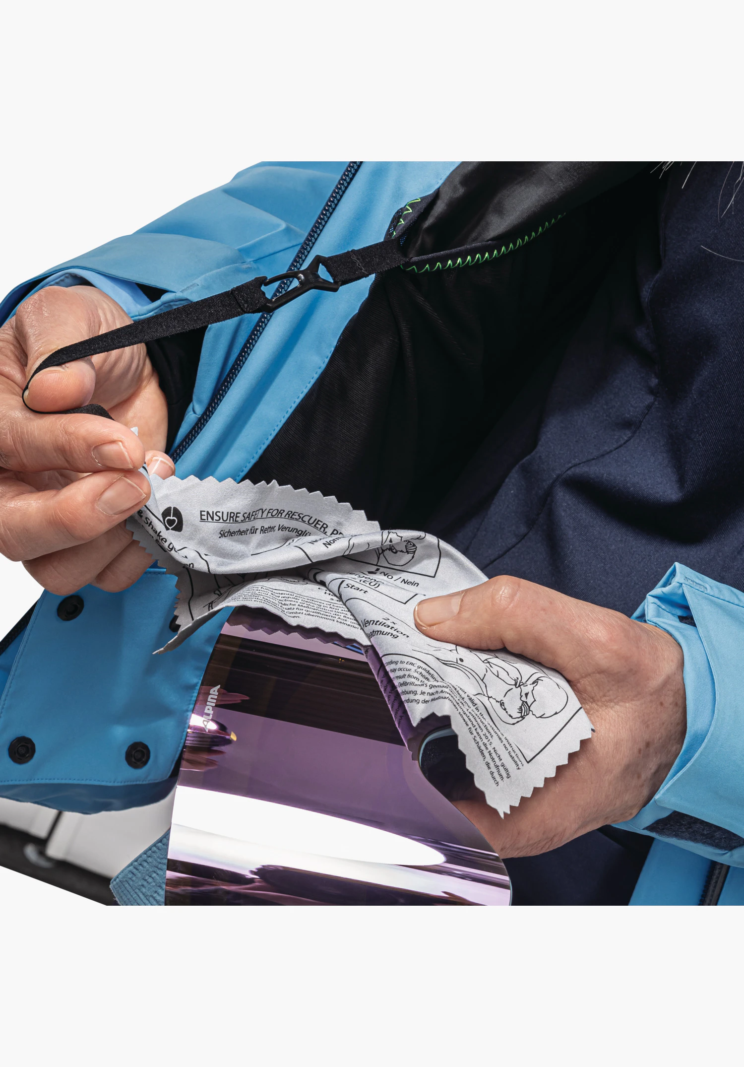 Jacket Style Trifex WMS, la chiffonnette pour lunettes intégrée avec consignes de sécurité imprimées sur une attache élastique, utilisée sur un écran de masque. Veste technique bleue en gros plan sur fond blanc.